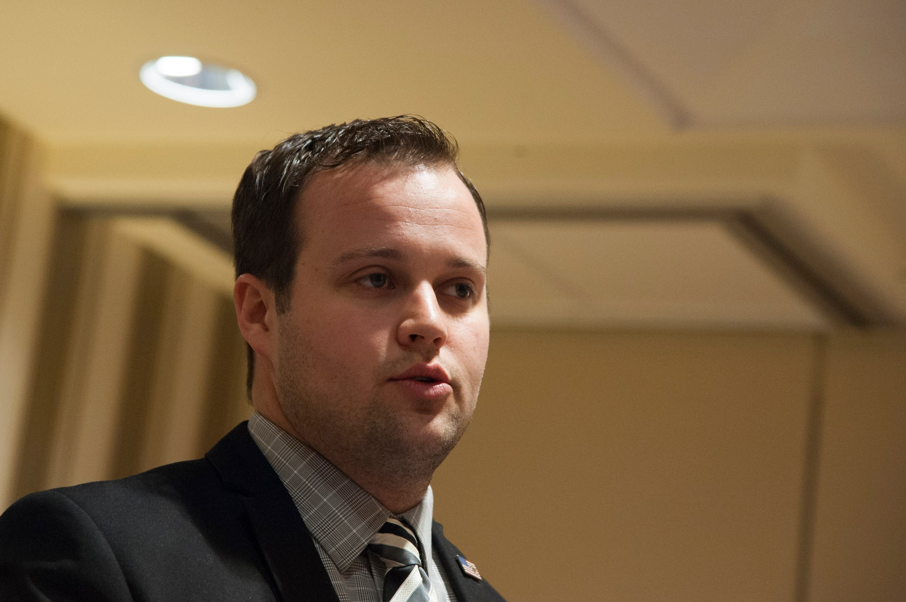 josh duggar in a suit and tie speaks at an indoor event