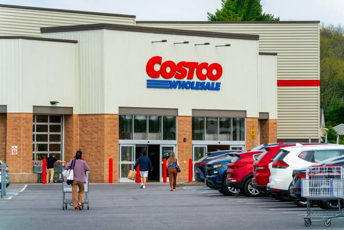 People entering and exiting a Costco Wholesale store, with cars successful  the parking lot