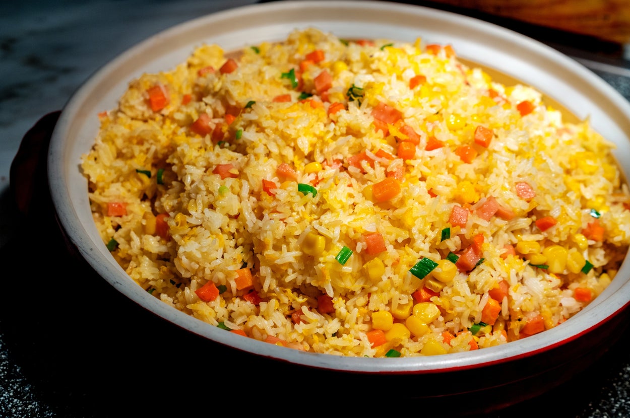 A bowl of fried rice with diced vegetables, including carrots and corn, garnished with green onions