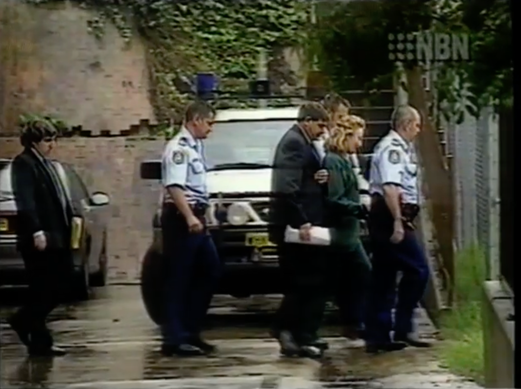 Group of constabulary  officers escort a handcuffed idiosyncratic  adjacent   a parked constabulary  conveyance  connected  a bedewed  street