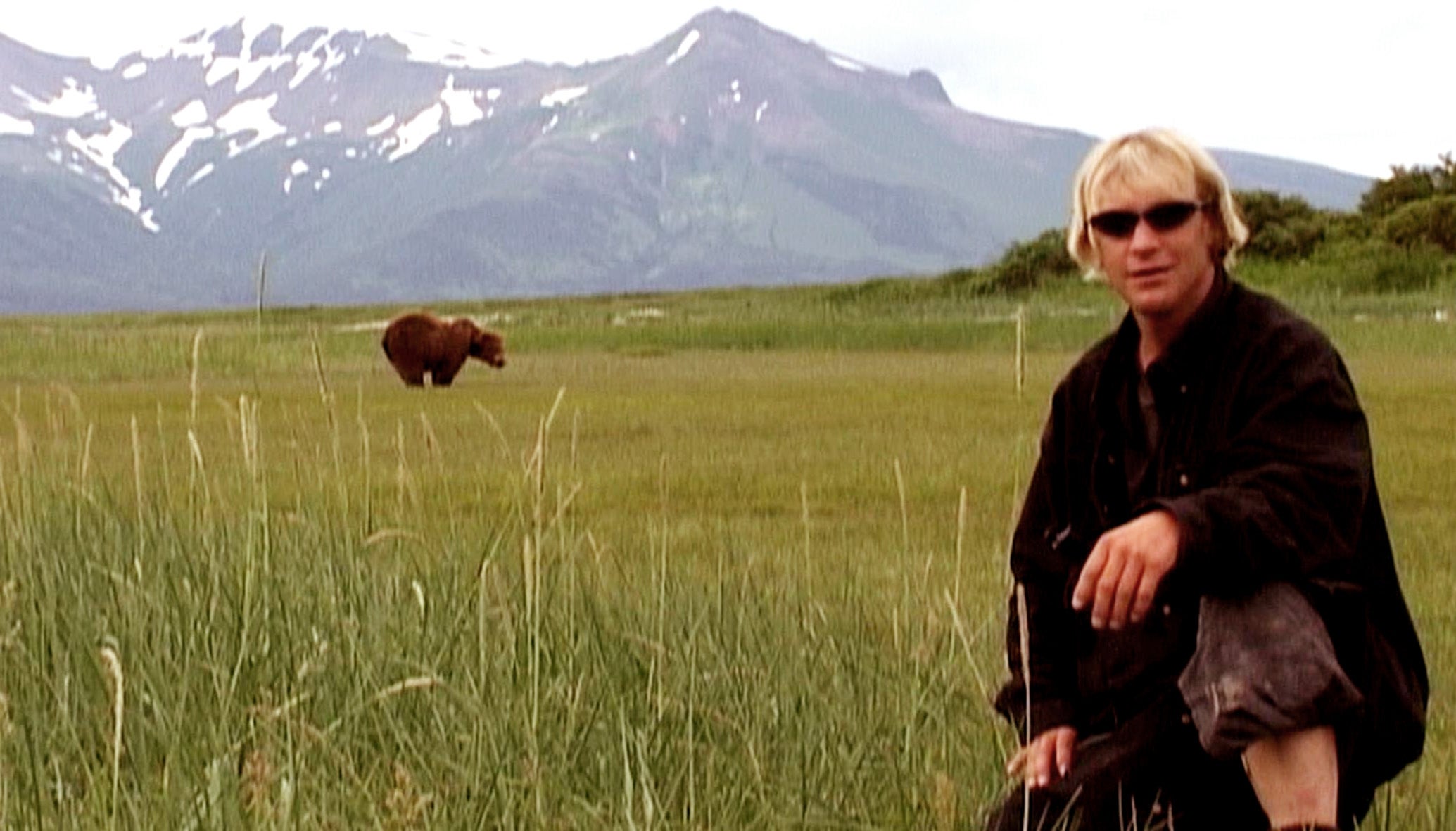 Person crouching successful a grassy tract with a carnivore successful the distance, upland scope successful the background