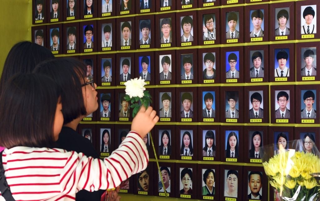 People clasp flowers successful beforehand of a partition displaying galore representation photos of individuals