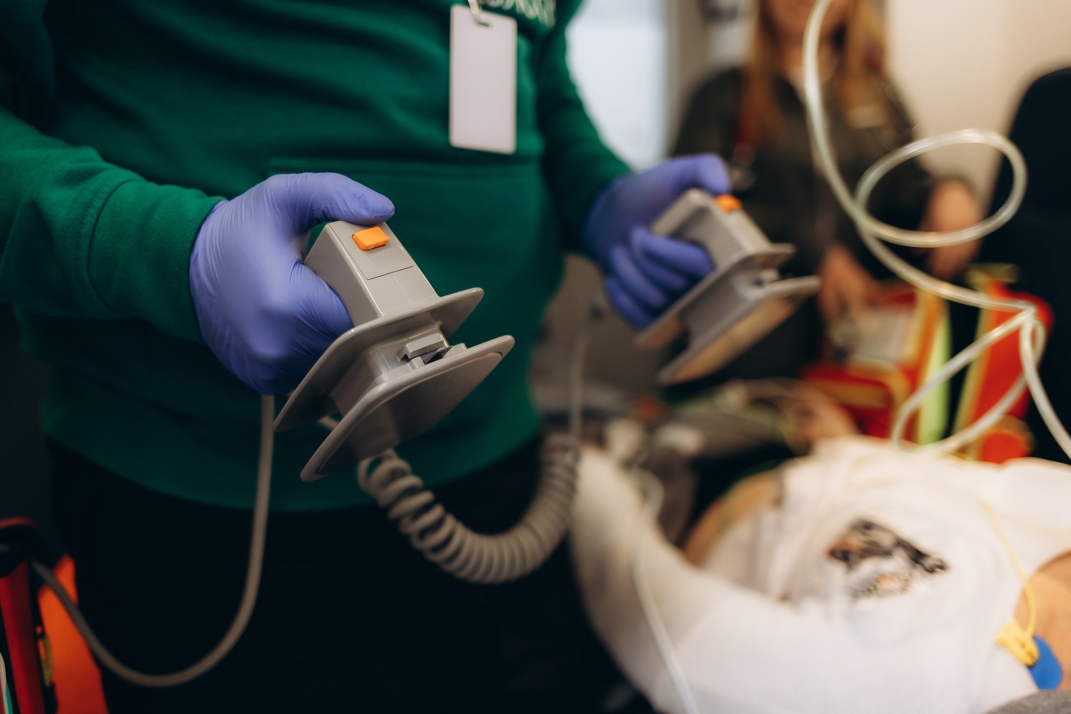 Person holding defibrillator paddles wearing gloves, adjacent a diligent connected a stretcher successful a aesculapian setting