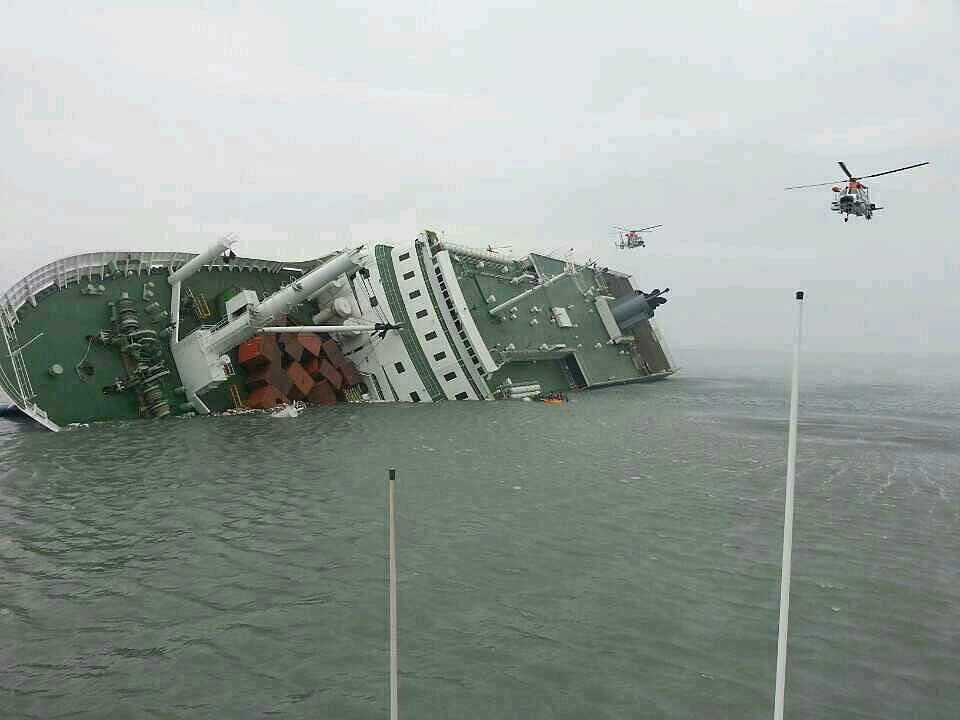 A ample ferry is tilted connected its broadside successful the h2o with 2 helicopters hovering above