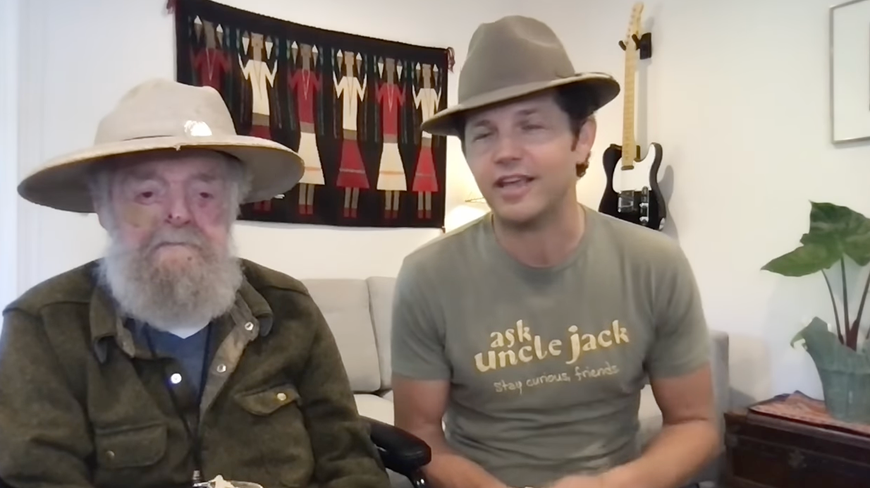 Two radical   seated, some  wearing wide-brimmed hats. The older idiosyncratic   has a agelong  beard, and the younger person's garment  reads "ask uncle jack."