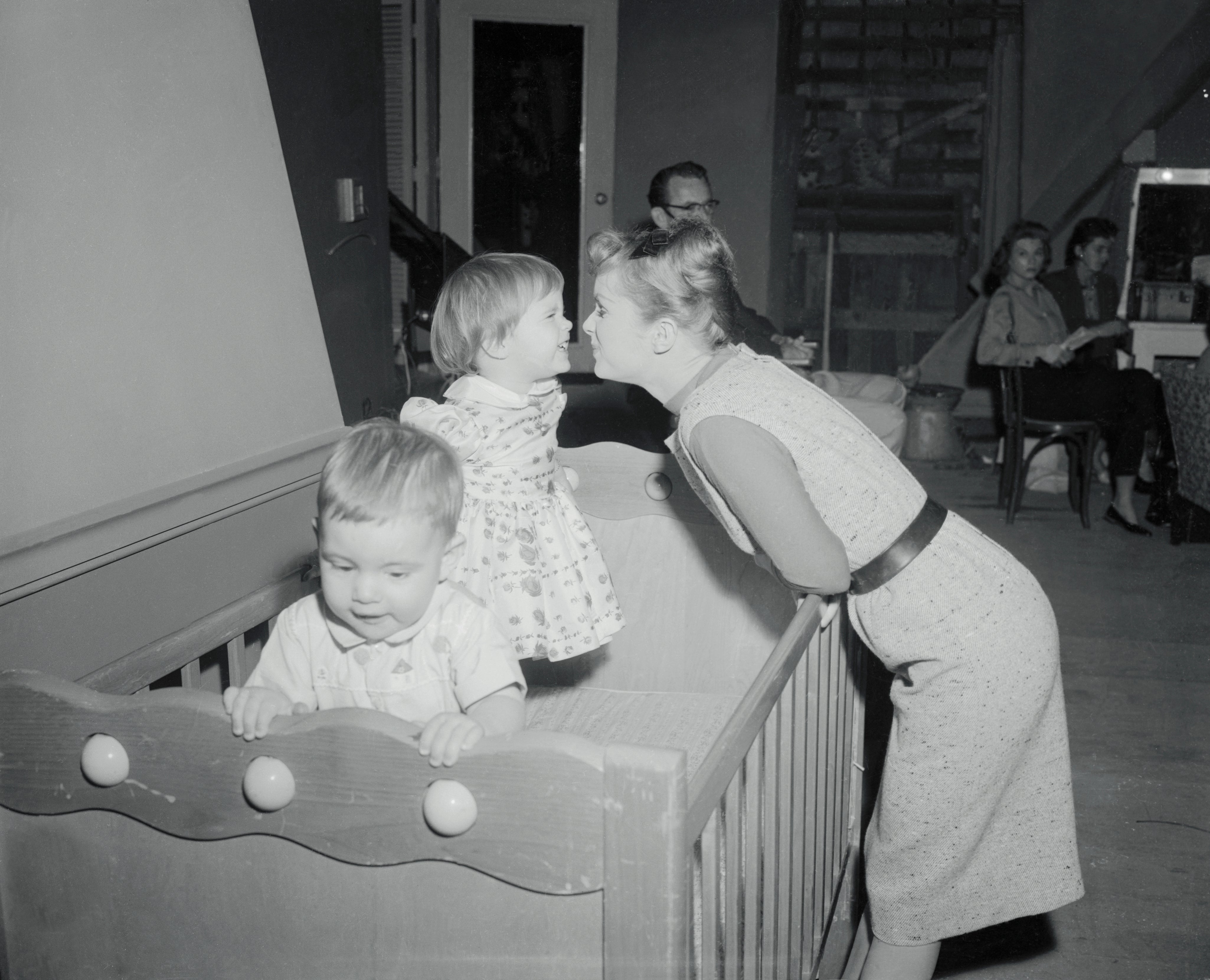 Actress Debbie Reynolds leans into a crib adjacent to girl Carrie connected set