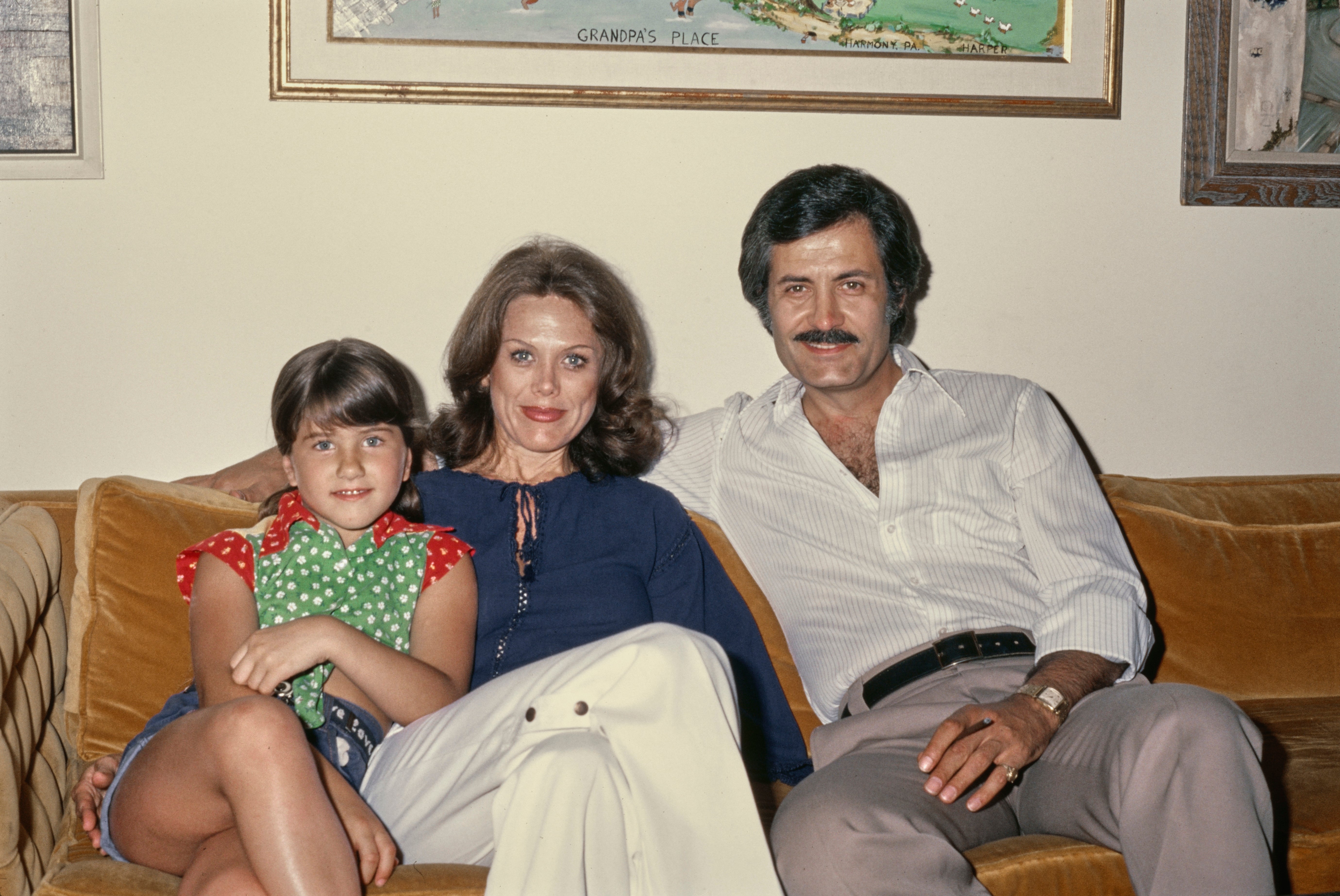 Young Jennifer Aniston sits with her parents connected a couch