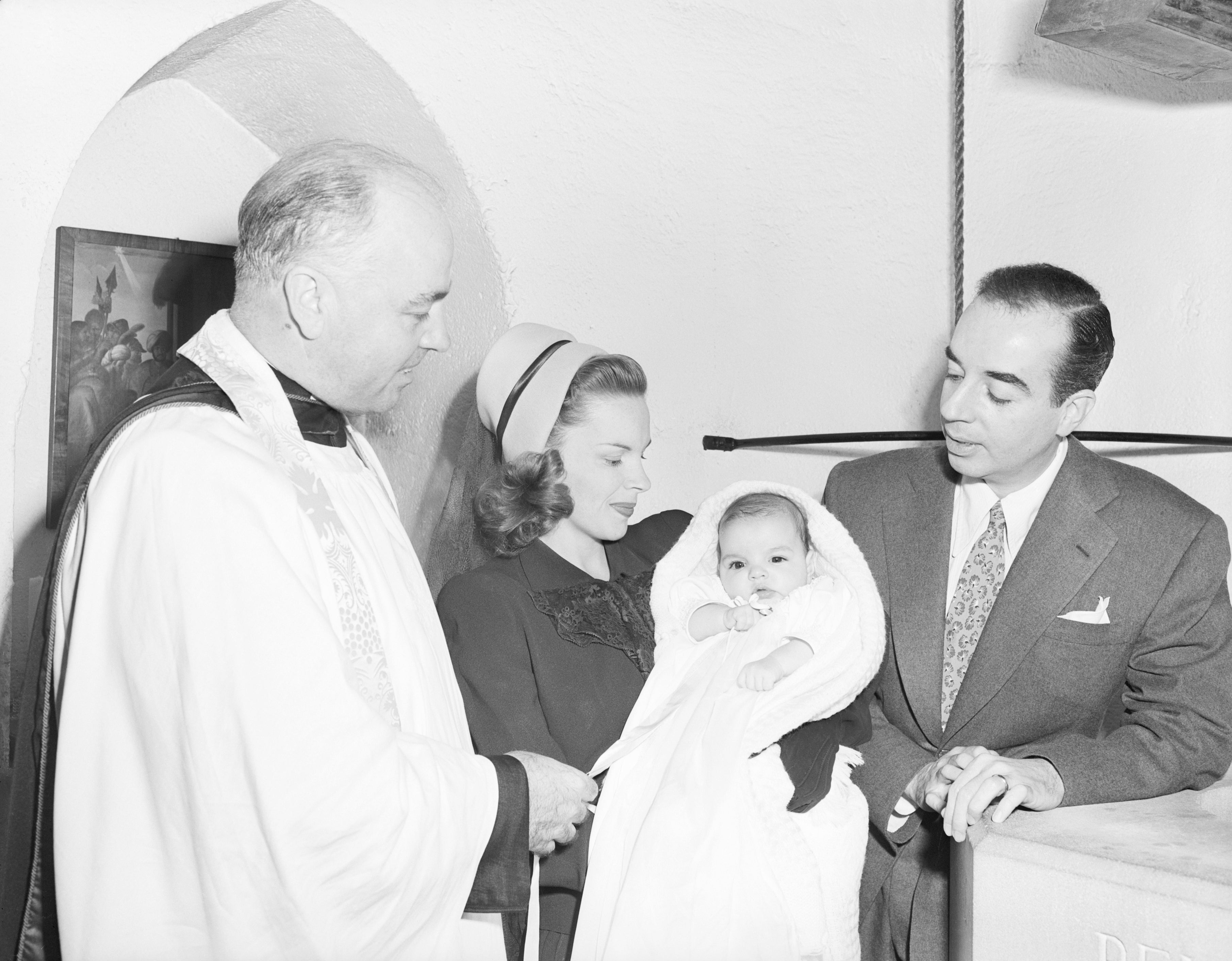 Judy Garland holds Liza portion Vincente and a clergyman look on