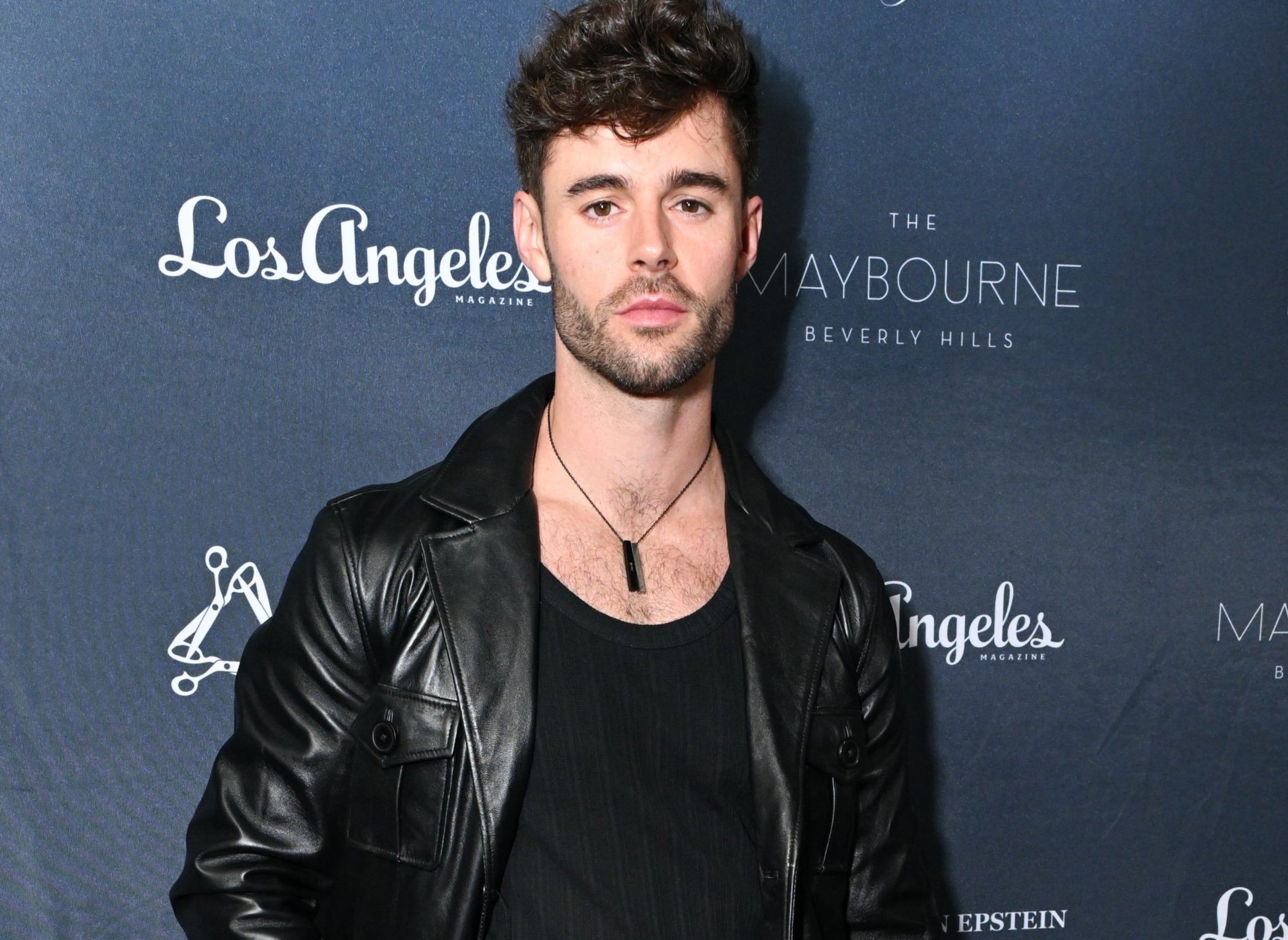 Person on red carpet in black leather jacket, black shirt, and black pants at a TV and movies event