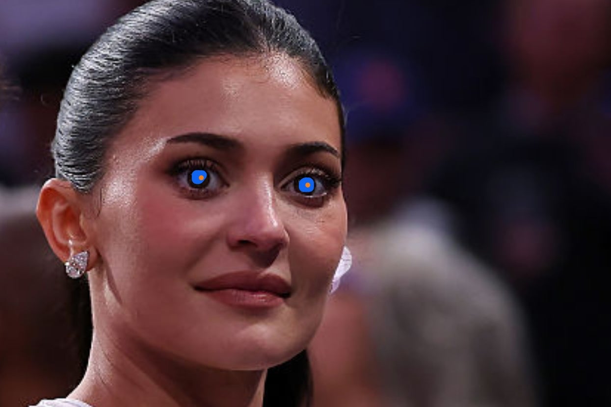 A person with tied-back hair is wearing diamond earrings and looking into the distance at an event; their eyes appear edited with bright lights