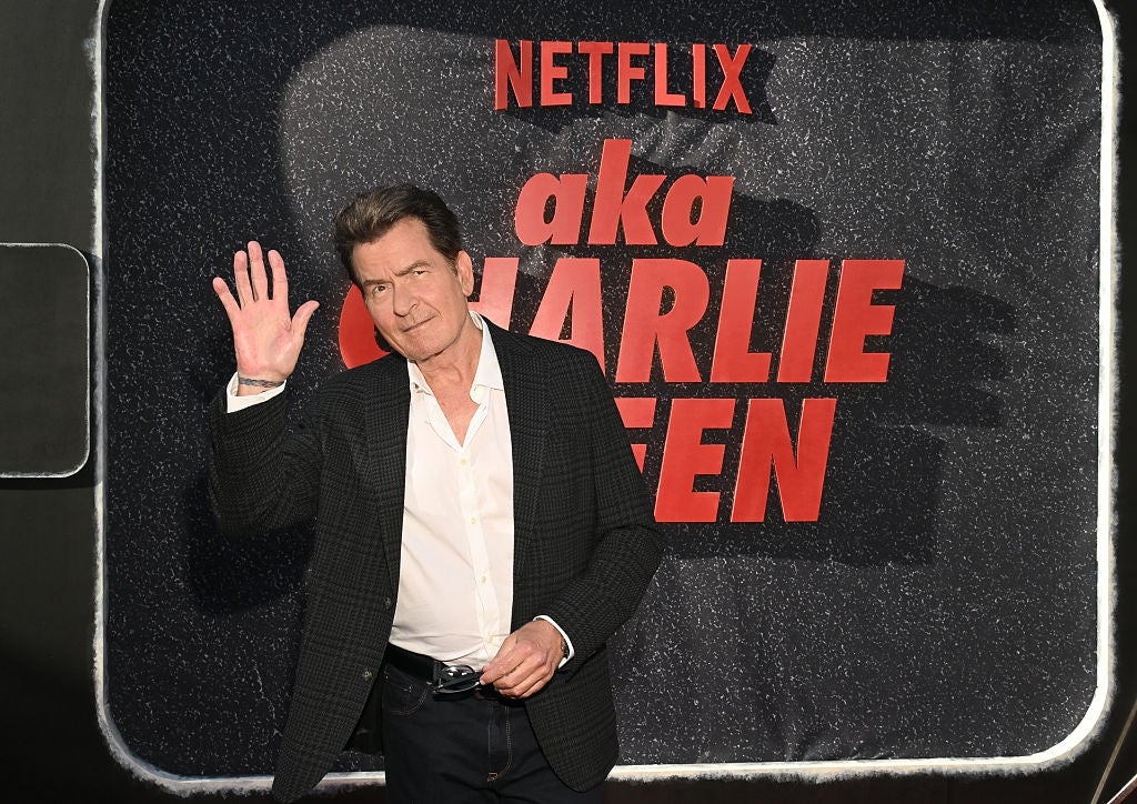 Man in a black suit and white shirt poses on a red carpet in front of a Netflix event backdrop