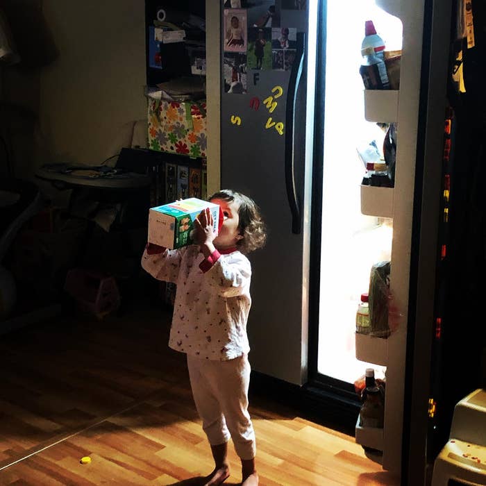Child drinking from a carton adjacent   an unfastened  refrigerator successful  a kitchen
