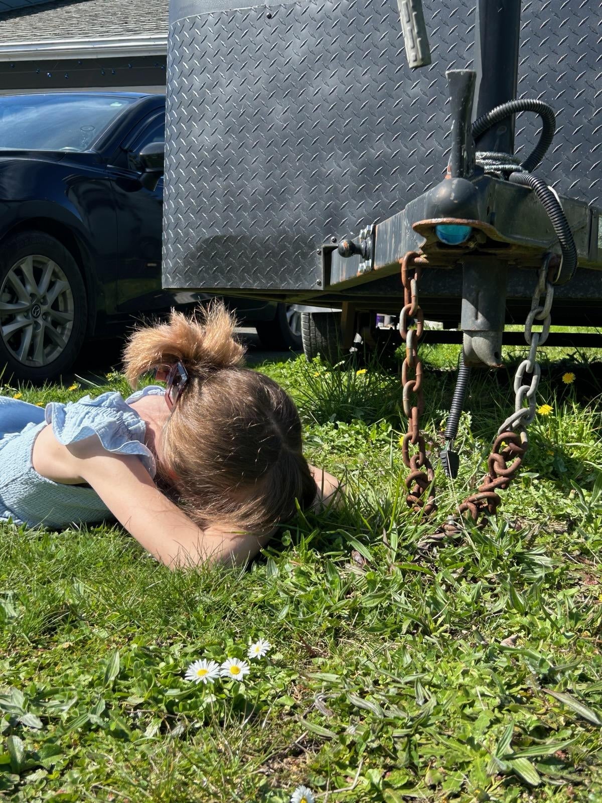 Child lying connected  writer  adjacent   a trailer hitch chain, shielding look   with arms