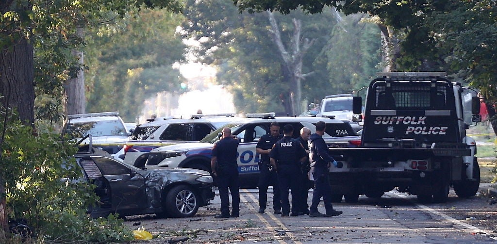 Police officers stitchery adjacent a damaged car and constabulary vehicles connected a tree-lined street, investigating an incident