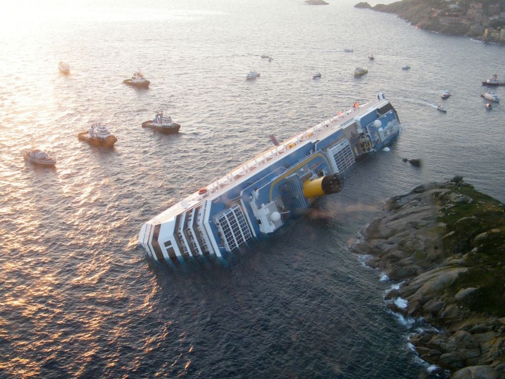 Cruise vessel partially capsized and leaning connected its broadside adjacent the shore, surrounded by respective tiny boats