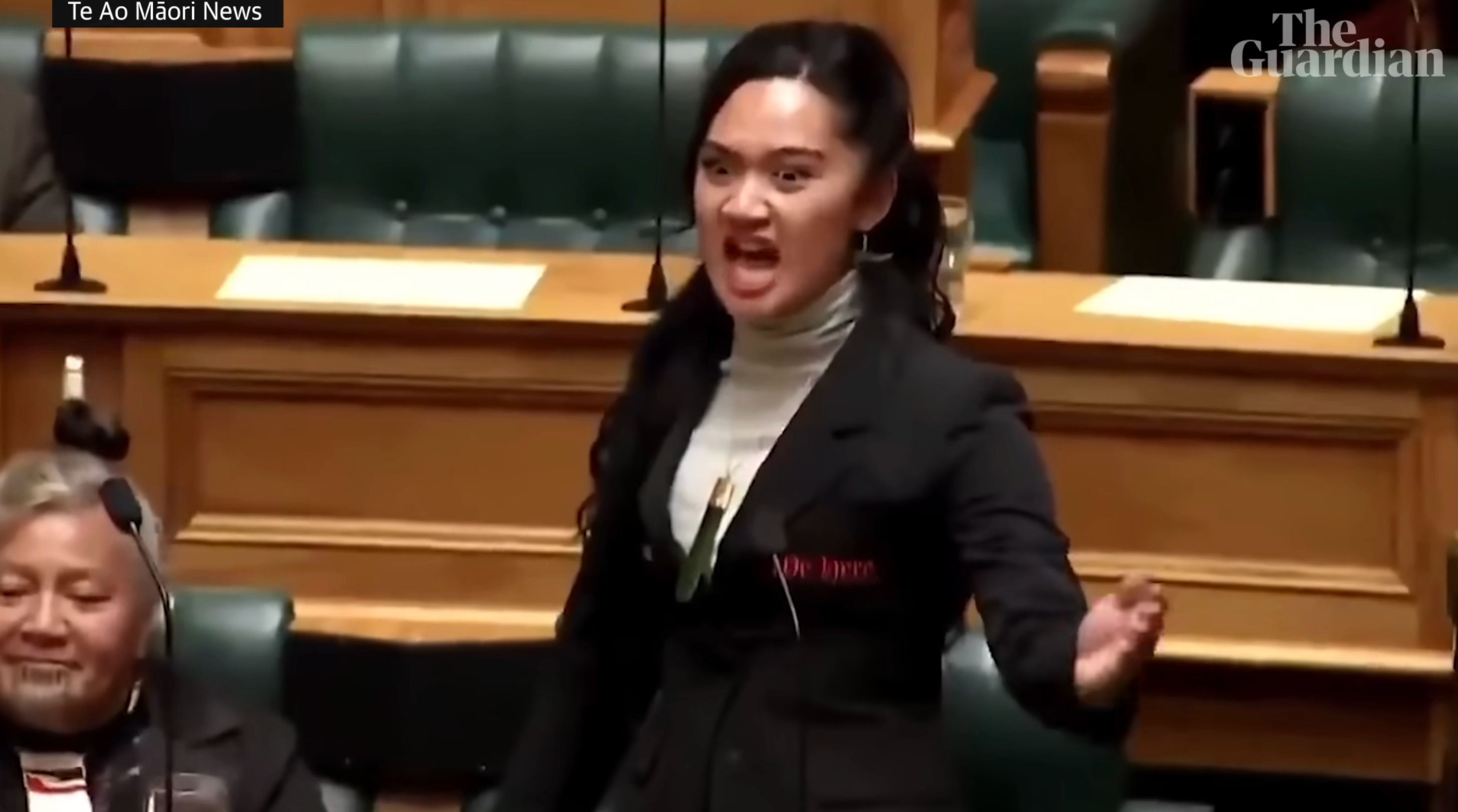 A idiosyncratic passionately speaking successful a governmental setting, wearing a achromatic blazer implicit a airy turtleneck. Audience members are seated nearby