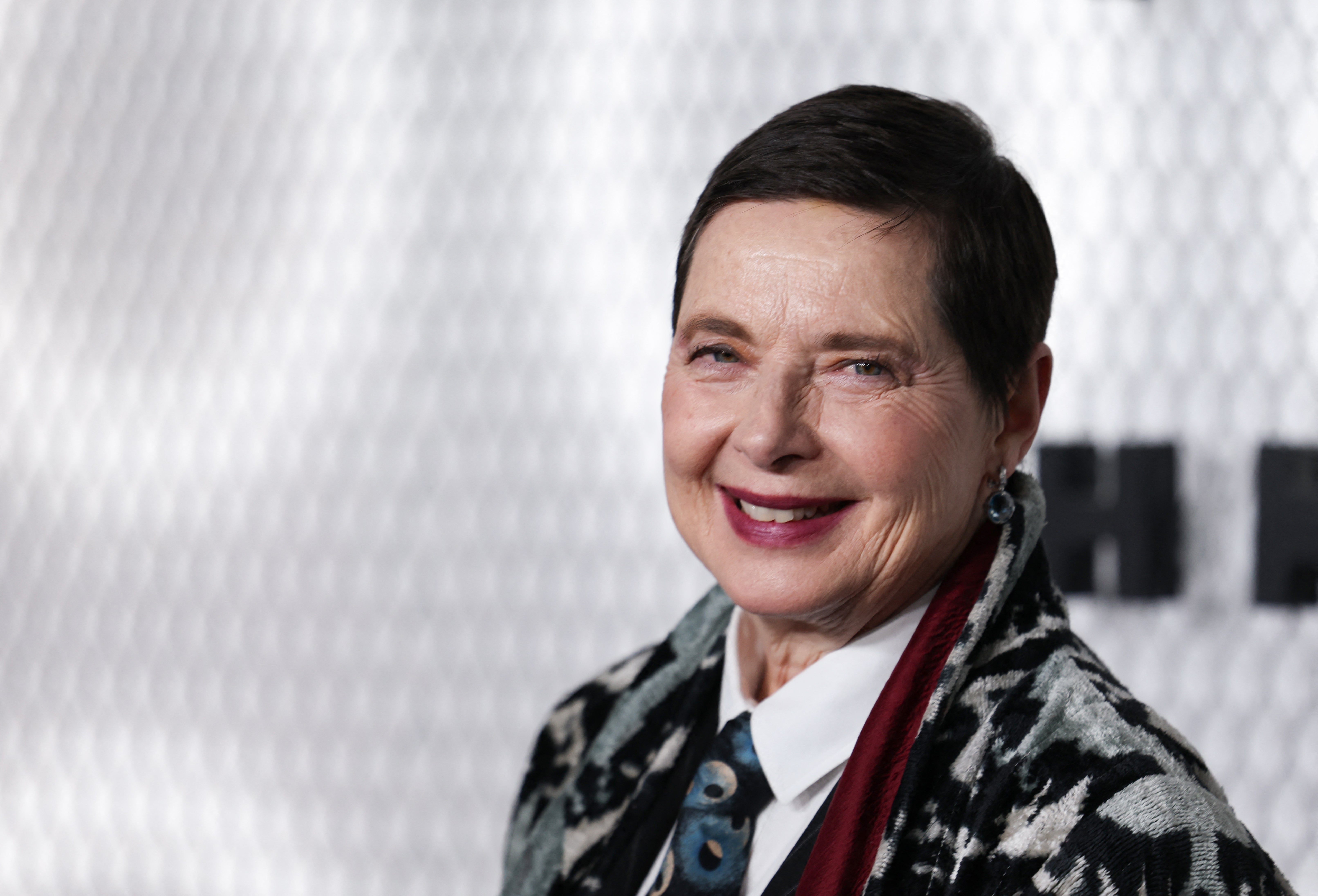 Isabella Rossellini wearing a patterned overgarment implicit a necktie and shirt, lasting against a patterned background