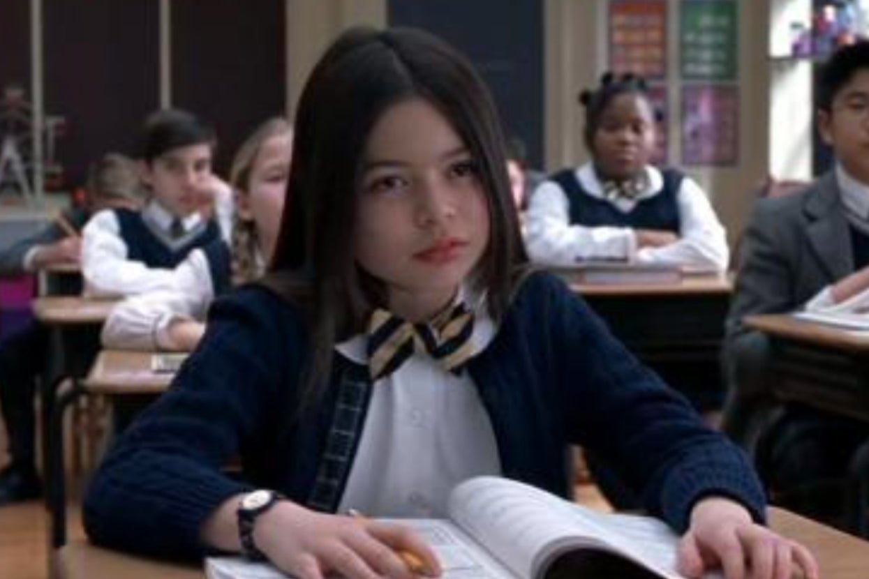 Miranda Cosgrove as a student in "School of Rock" in a classroom sits attentively at a desk with an open book, looking annoyed