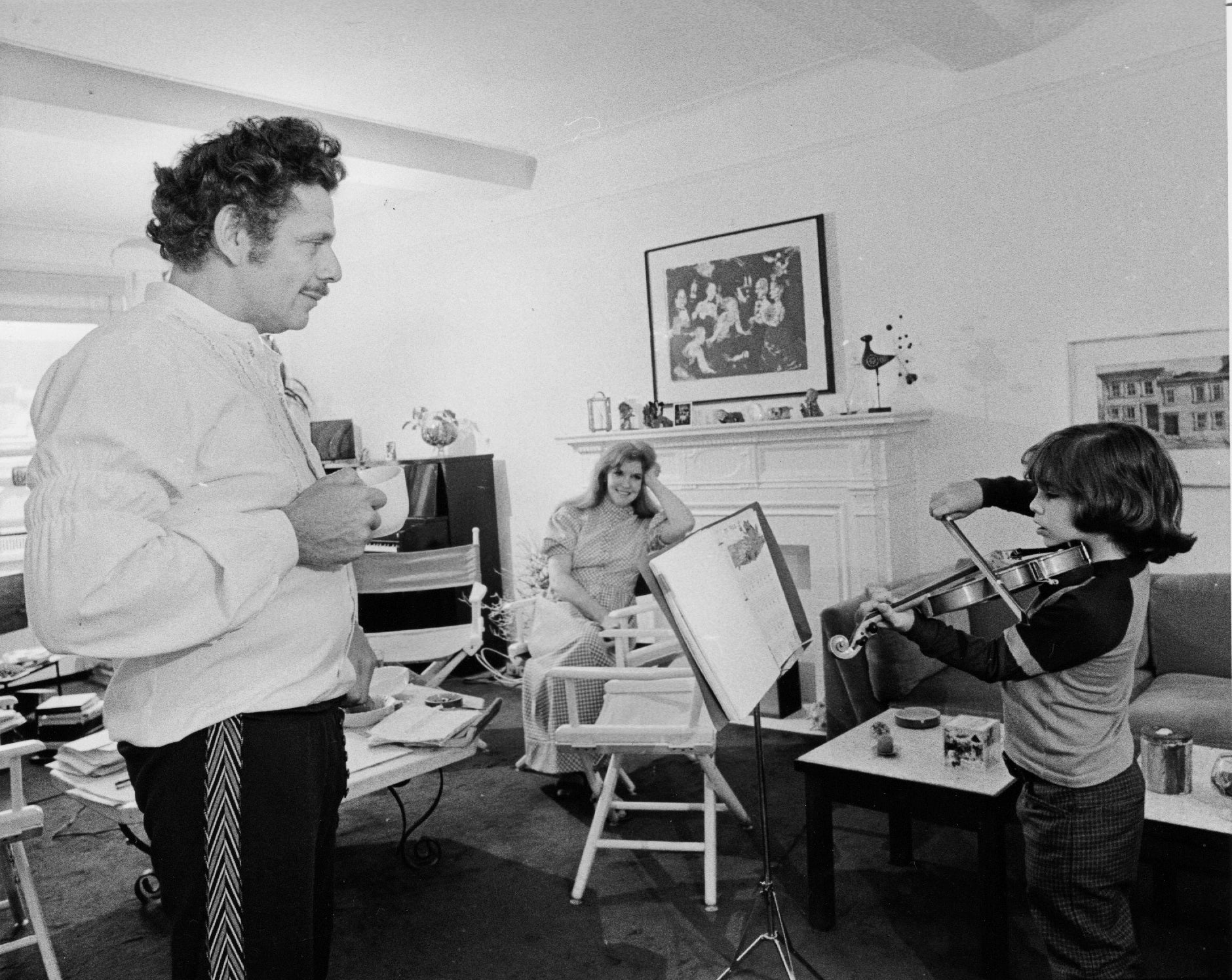 Jerry watches arsenic Ben plays the violin successful a cozy surviving room, portion Anne sits and observes from a seat adjacent the fireplace