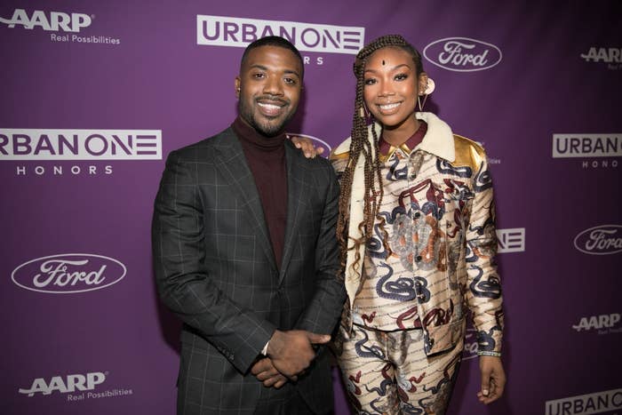 Two people on the red carpet. One in a plaid suit, the other in a vibrant patterned outfit