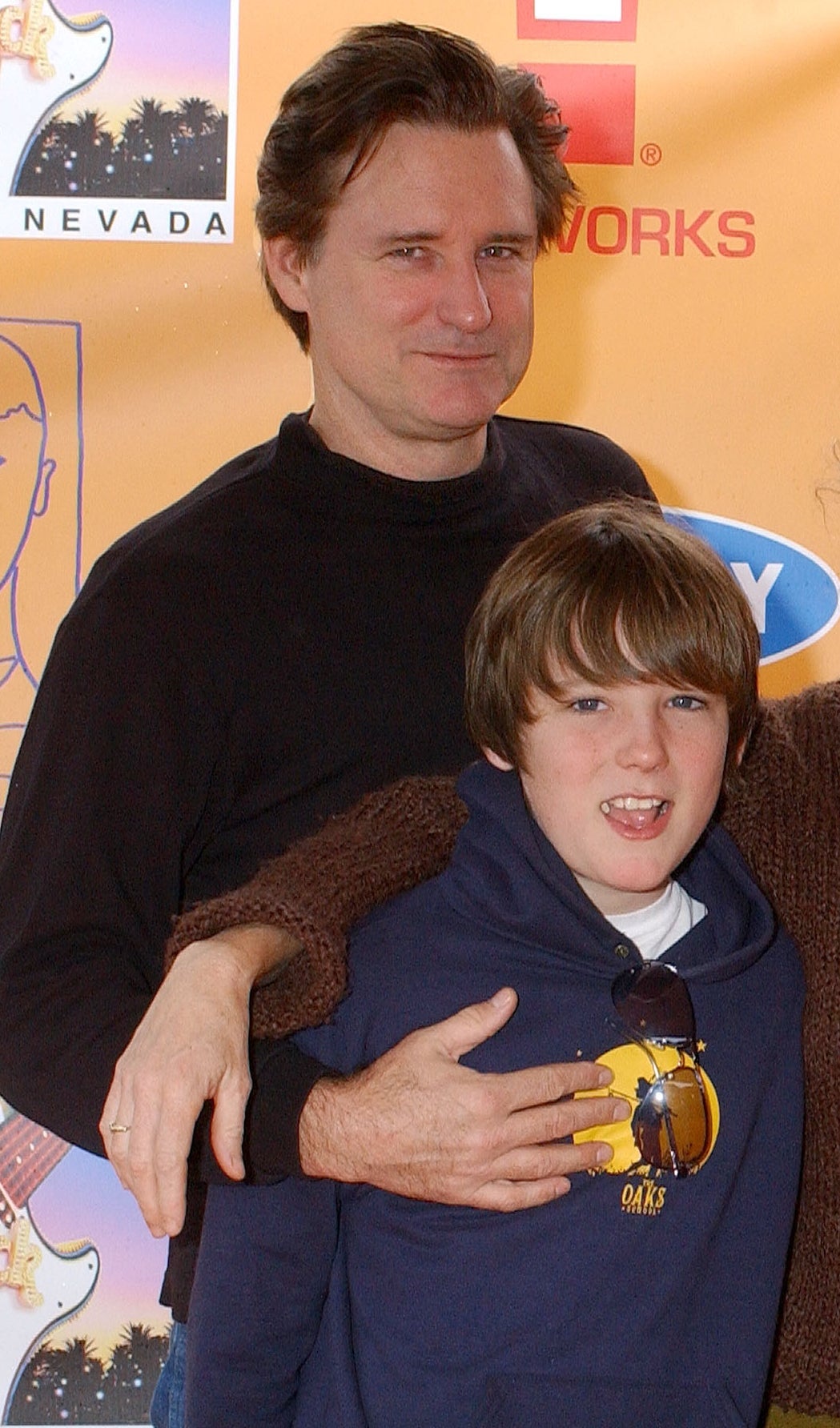 Bill Pullman wearing a acheronian sweater smiling with his limb astir a Lewis successful a hoodie astatine a casual event