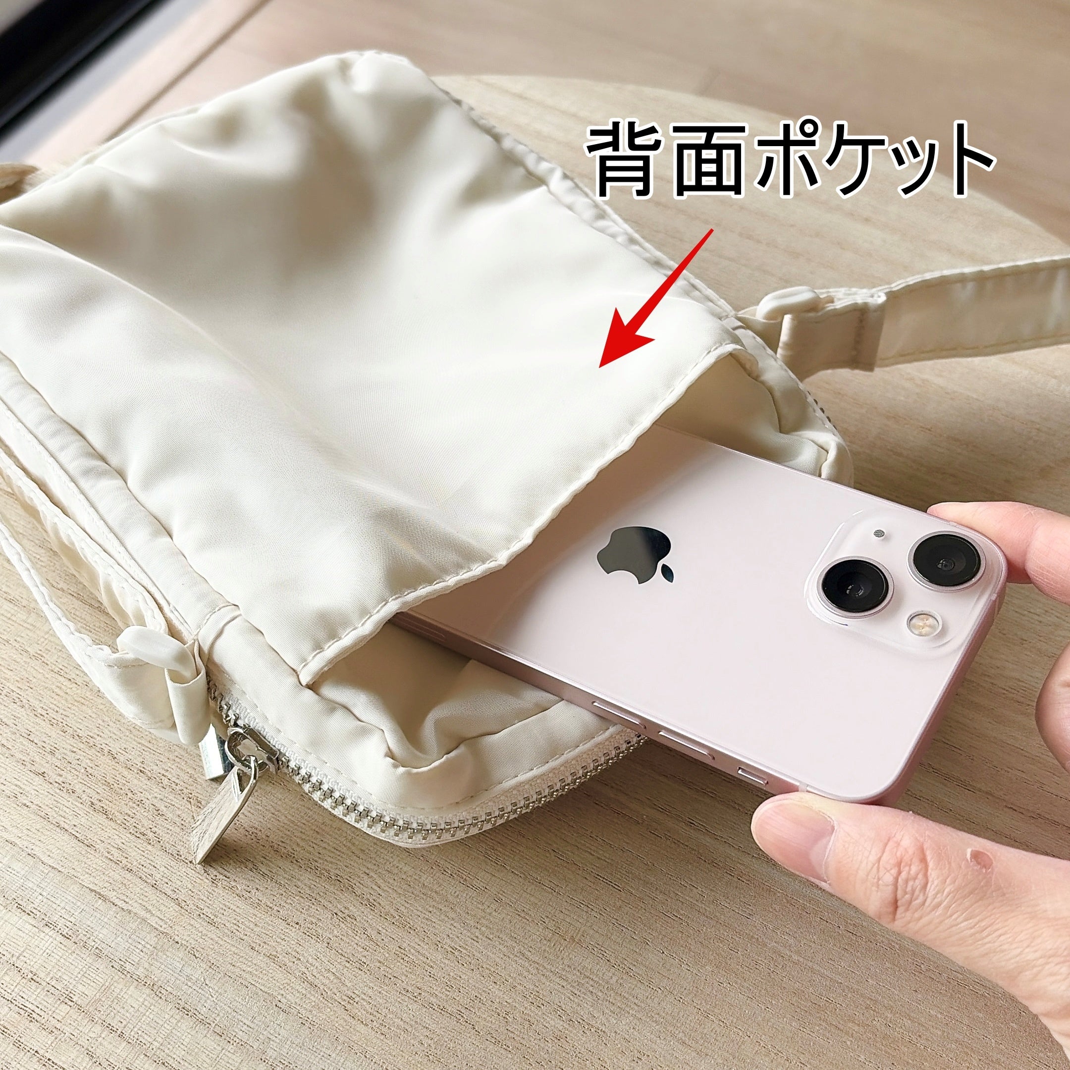 3COINS（スリーコインズ）「はっ水ミニショルダーバッグ」白いショルダーバッグにスマートフォンを入れる手元の写真。布地製で、外出時に便利そう。