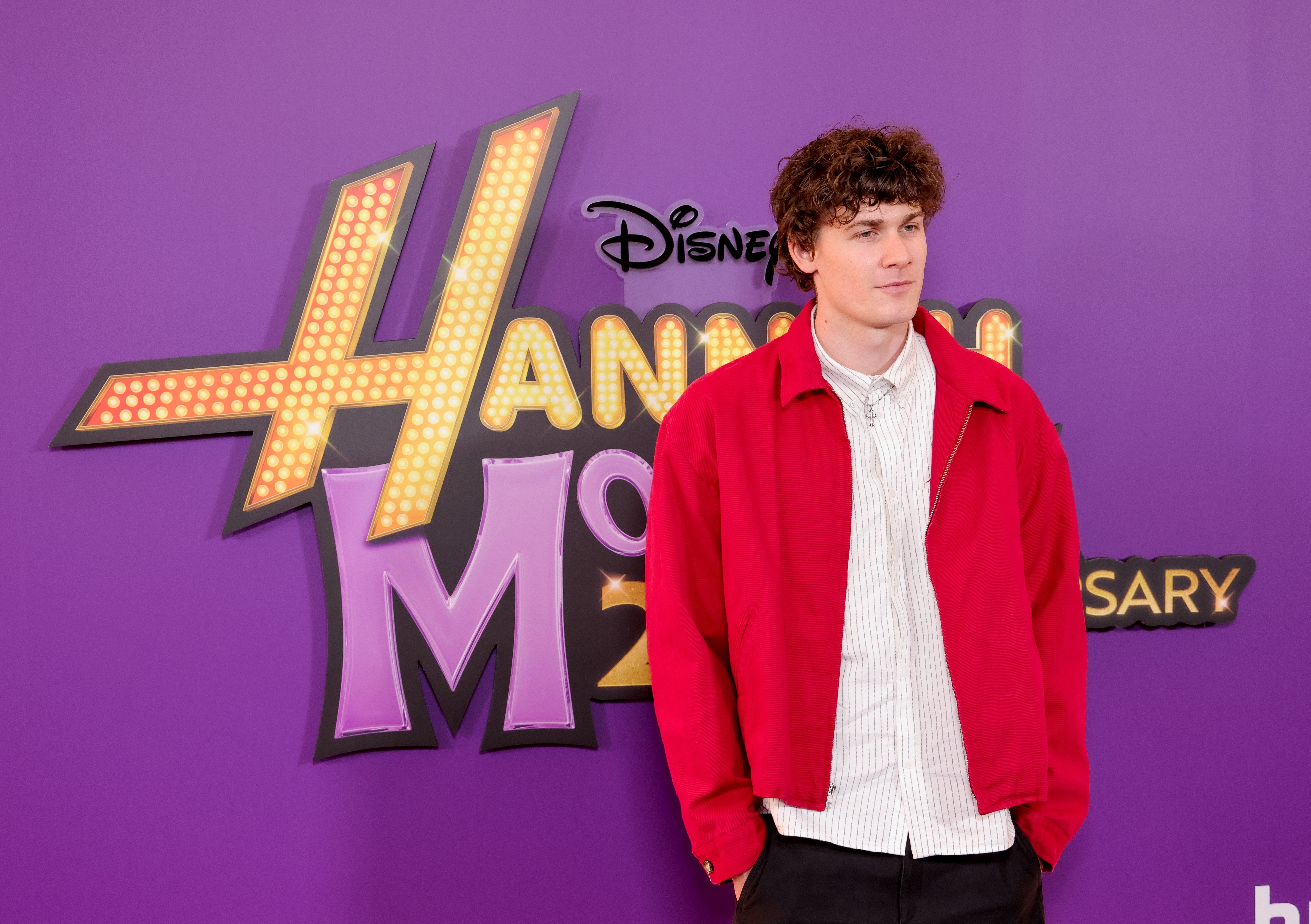 Person in a red jacket poses at an event celebrating a TV show's 20th anniversary, standing in front of the show's logo