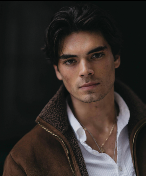 Person in a collared shirt and jacket, looking directly at the camera with a thoughtful expression