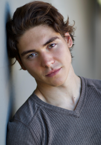 Person with wavy hair wearing a ribbed V-neck shirt gazes softly at the camera