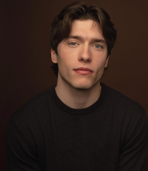 Person posing against a dark background, wearing a simple black top
