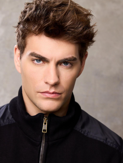 Person with styled short hair, wearing a black jacket, looking directly into the camera against a plain background