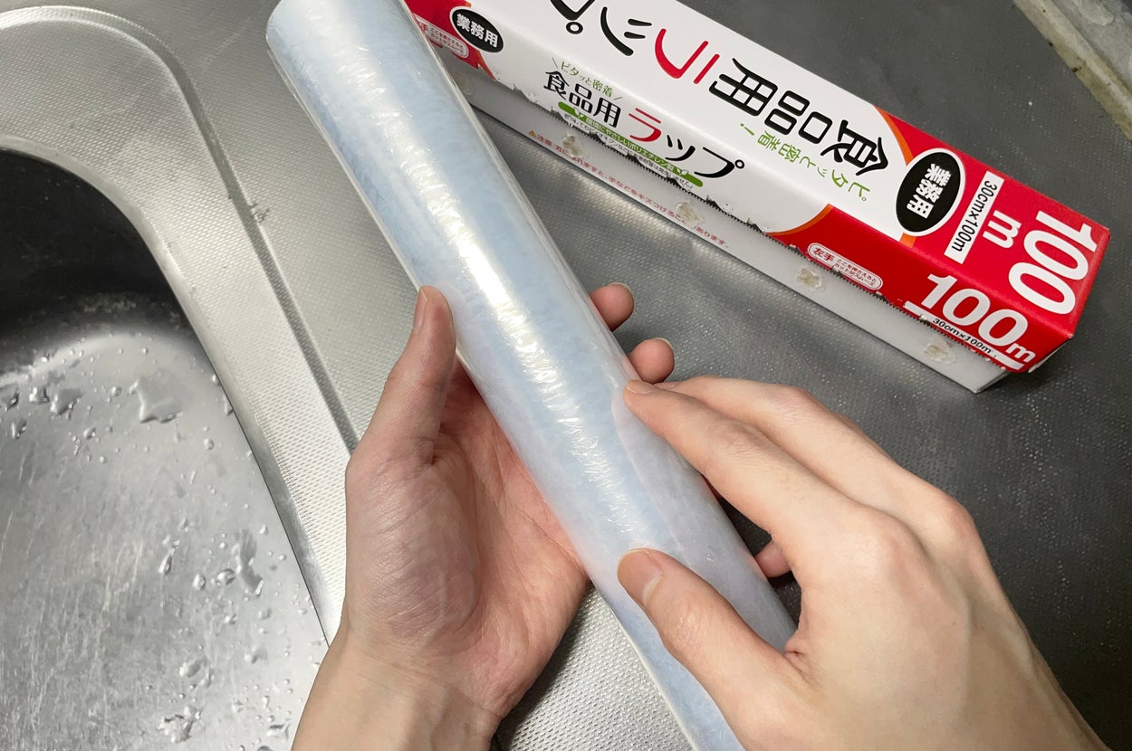 人の手が、シンクの横で食品用ラップを持っている様子。
