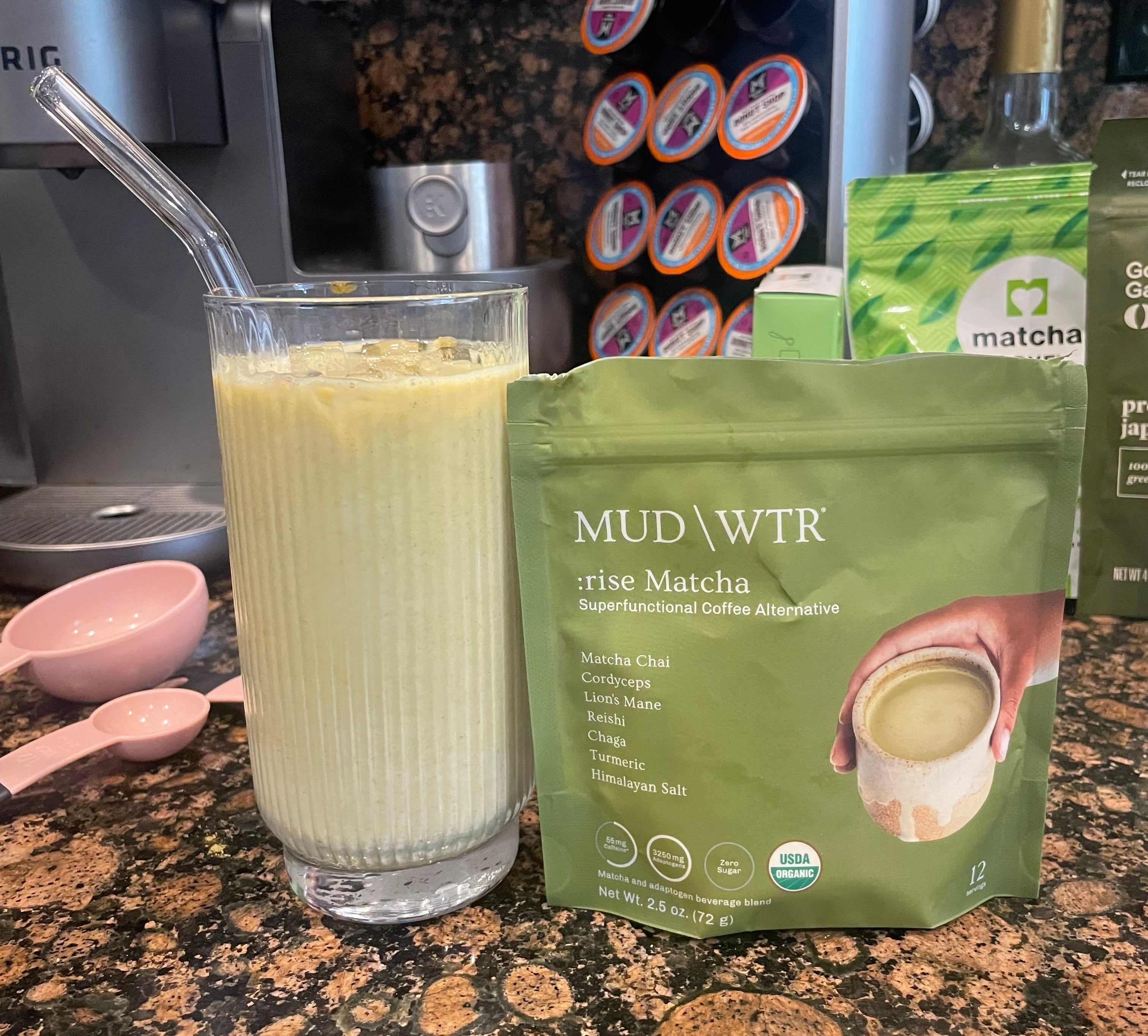 Glass of matcha drink with a metal straw next to a Mud\Wtr rise matcha blend pouch on a kitchen counter