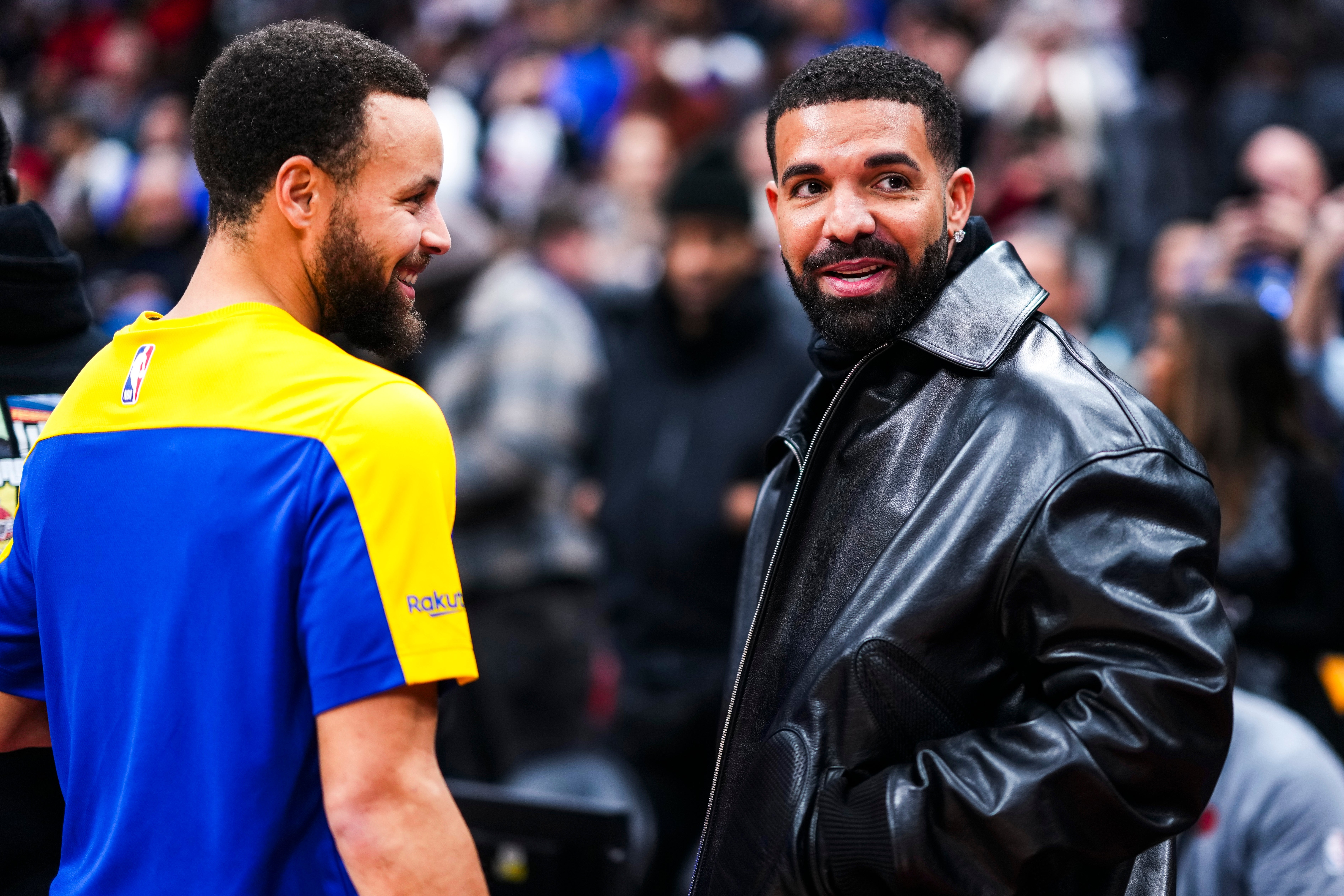 Two individuals are interacting at an event. One wears a sports jersey, the other a leather jacket. They appear to be enjoying the conversation