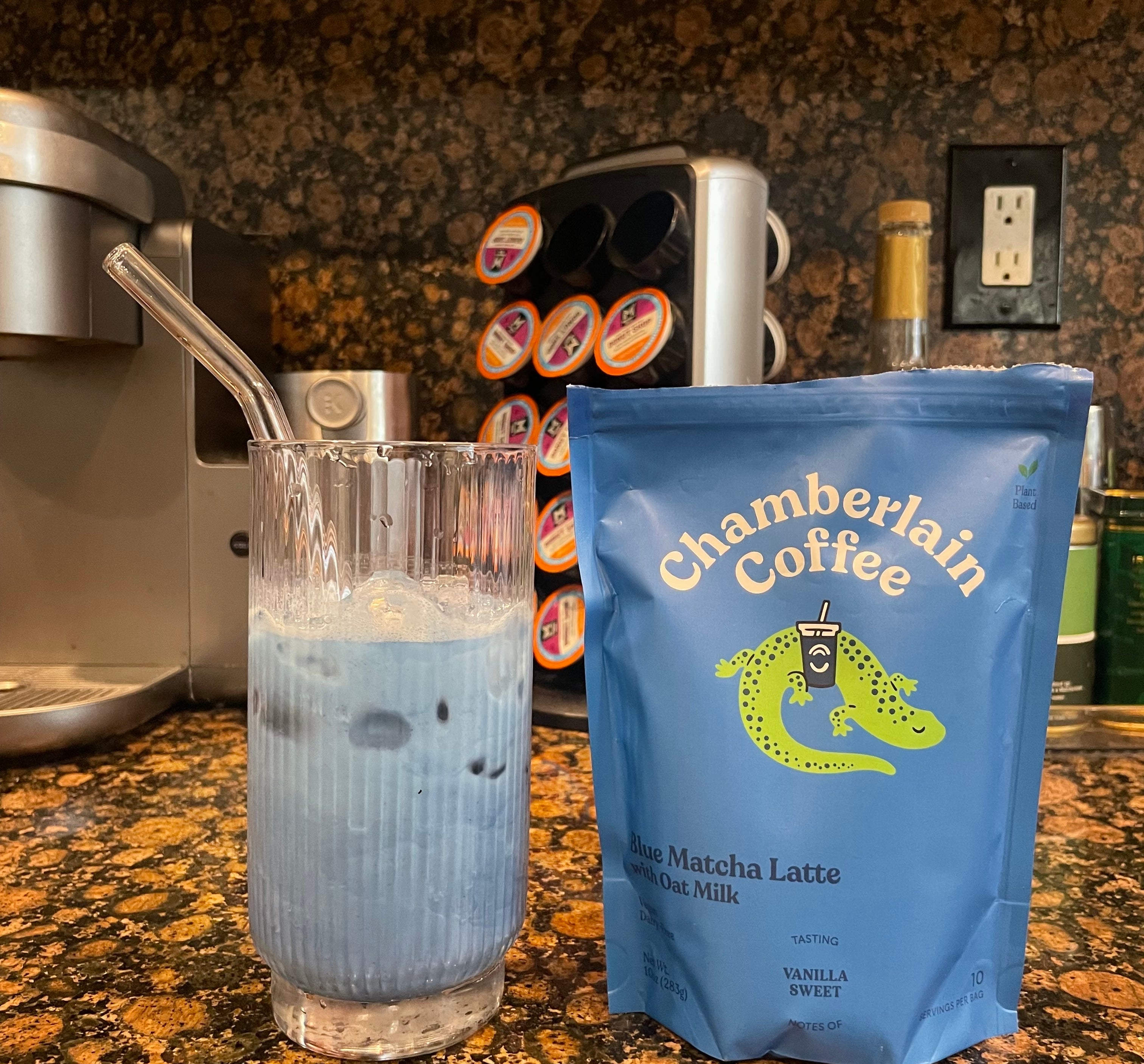 Glass of blue matcha latte with ice and straw beside a bag labeled "Chamberlain Coffee" on a kitchen counter