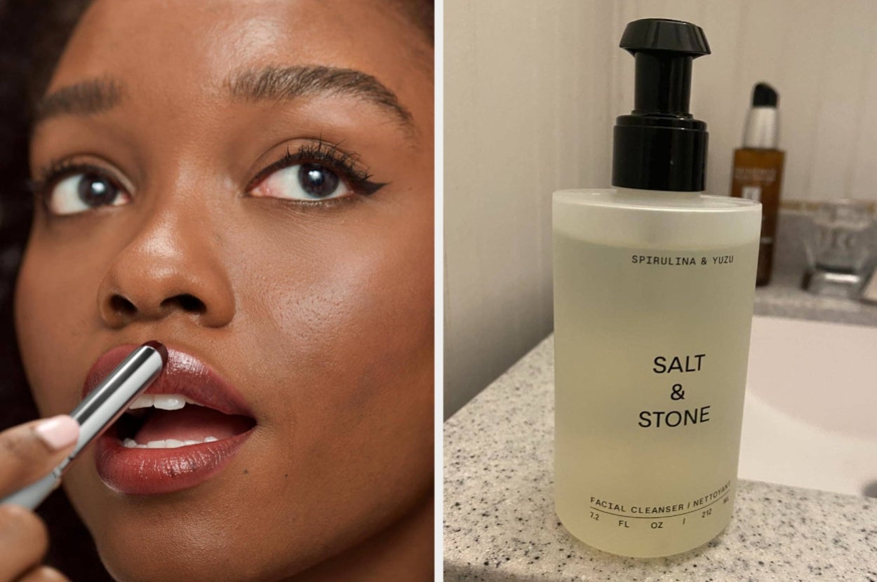 A person applies lipstick while holding a tube. Nearby, a bottle of Salt & Stone spirulina & yuzu facial cleanser is on a bathroom counter