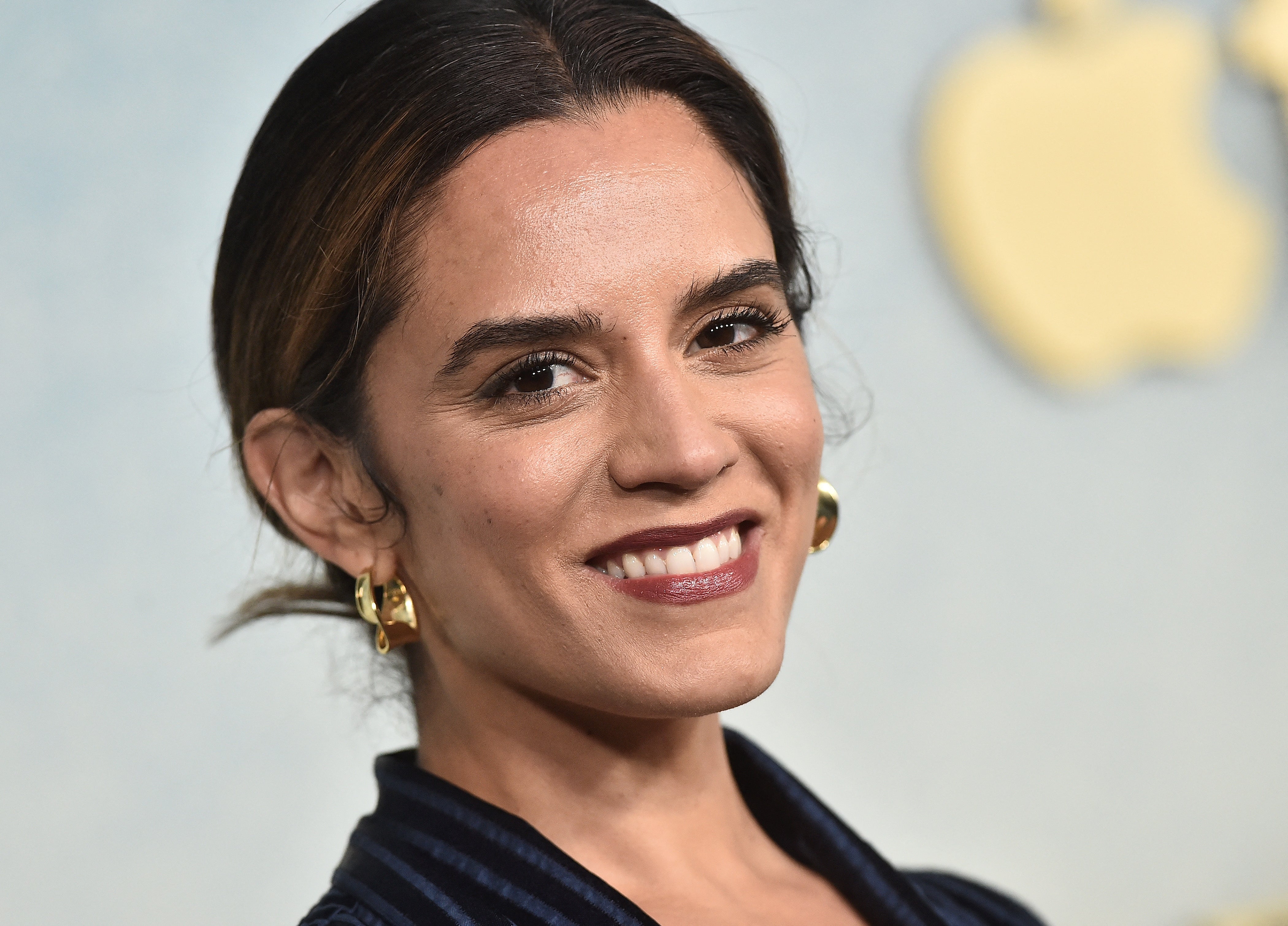 Person smiling, wearing golden  hoop earrings and a stylish textured outfit, astatine  a TV lawsuit   backdrop