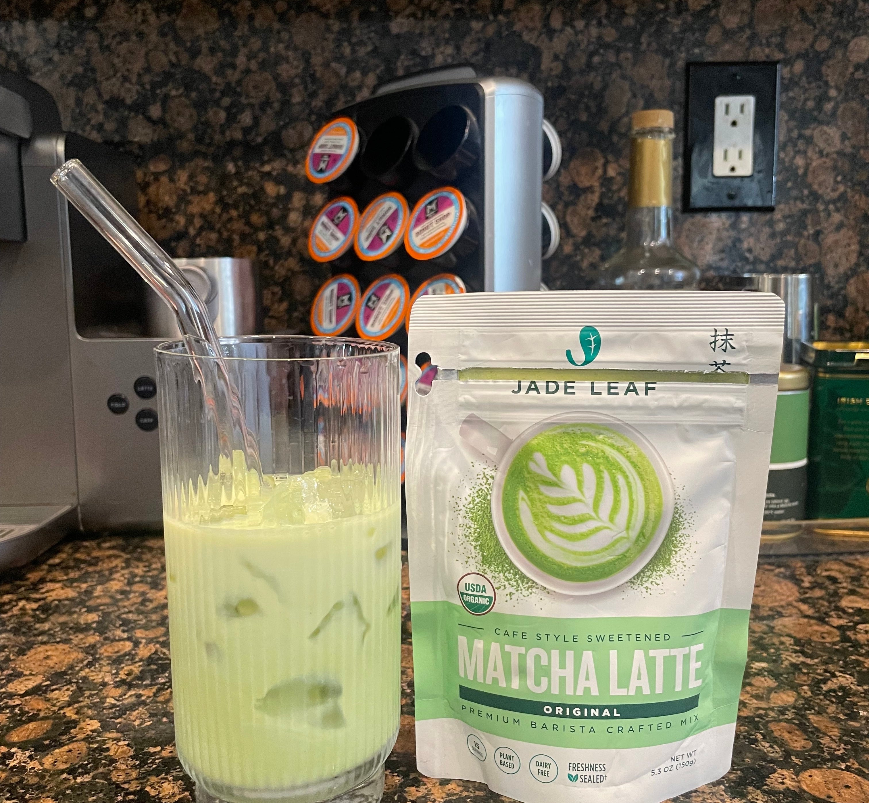 A glass of matcha latte with ice beside a bag of Jade Leaf Matcha Latte mix on a kitchen counter