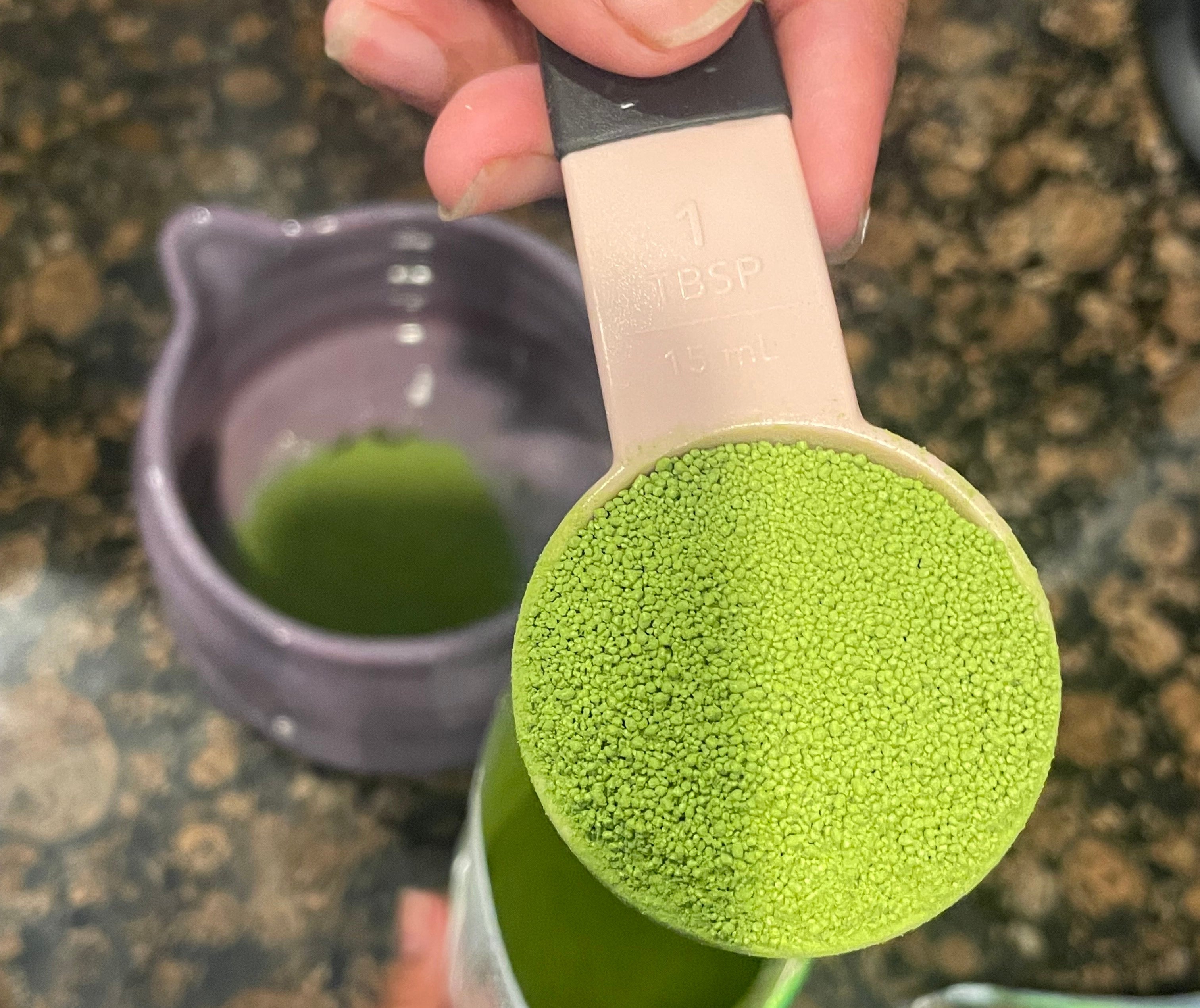 A hand holding a tablespoon of vibrant green matcha powder over a bowl