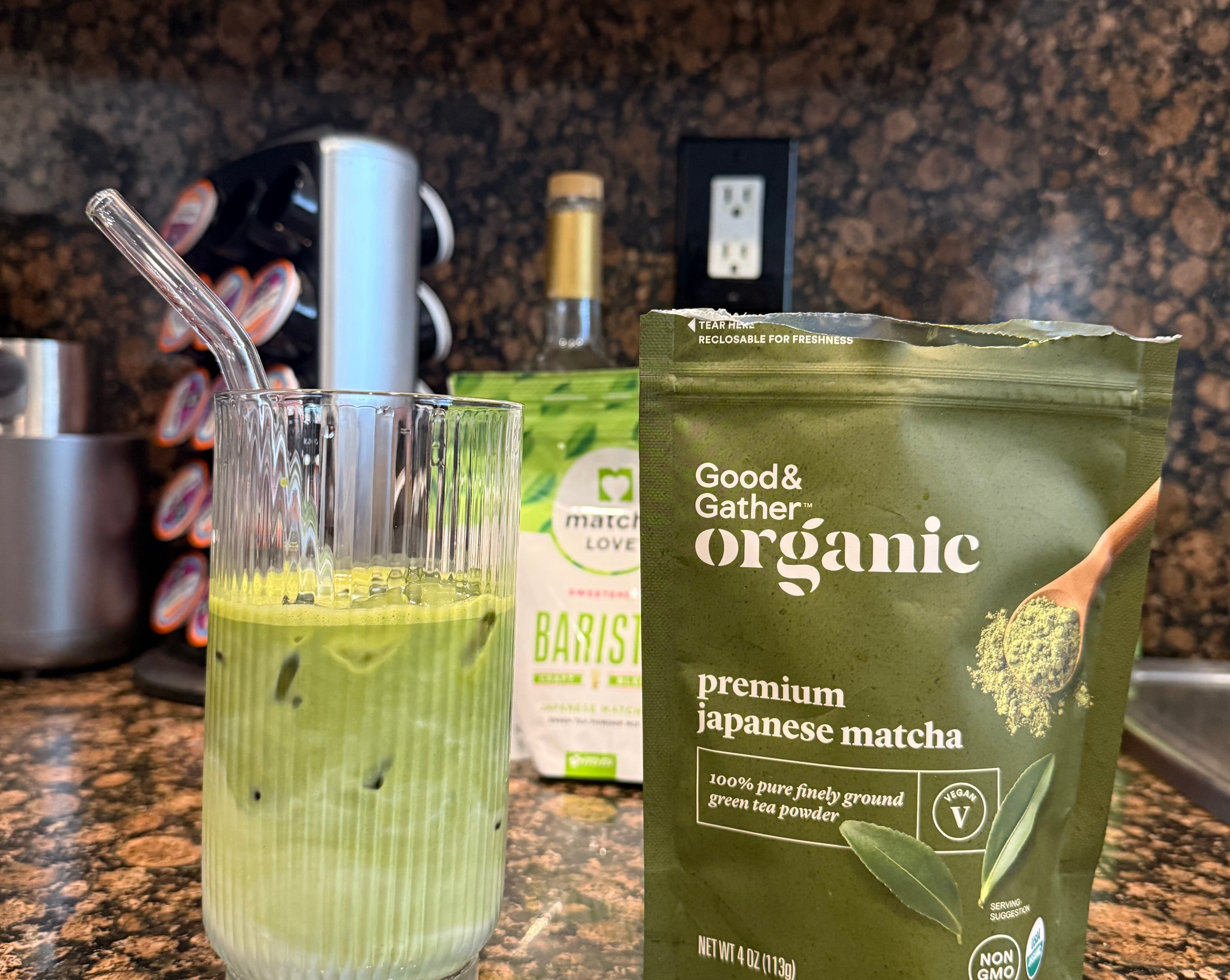 Iced matcha latte with a glass straw sits beside a bag of organic Japanese matcha on a kitchen counter