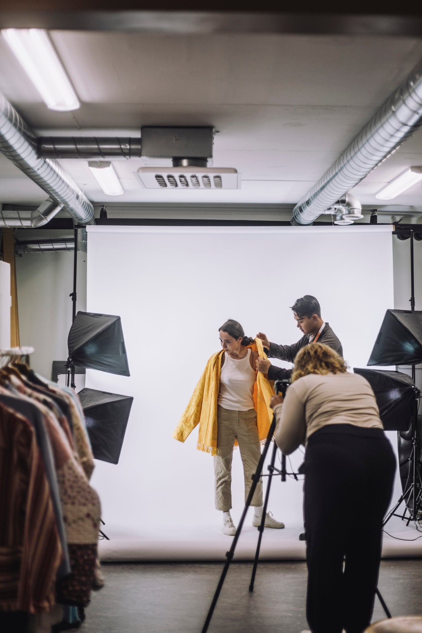 Photographer and assistant adjust a model's outfit during a photoshoot in a well-lit studio