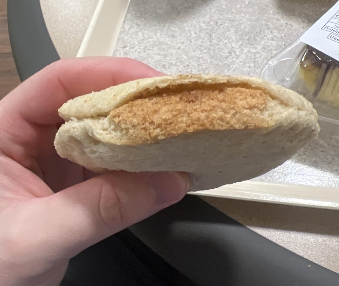 Sebuah tangan memegang sandwich yang terbuat dari dua potong roti dengan lapisan isian yang terlihat