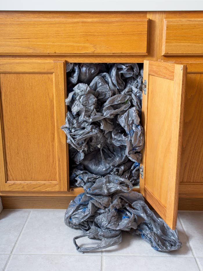 Cabinet overflowing with galore   crumpled integrative  bags, spilling retired  onto the floor