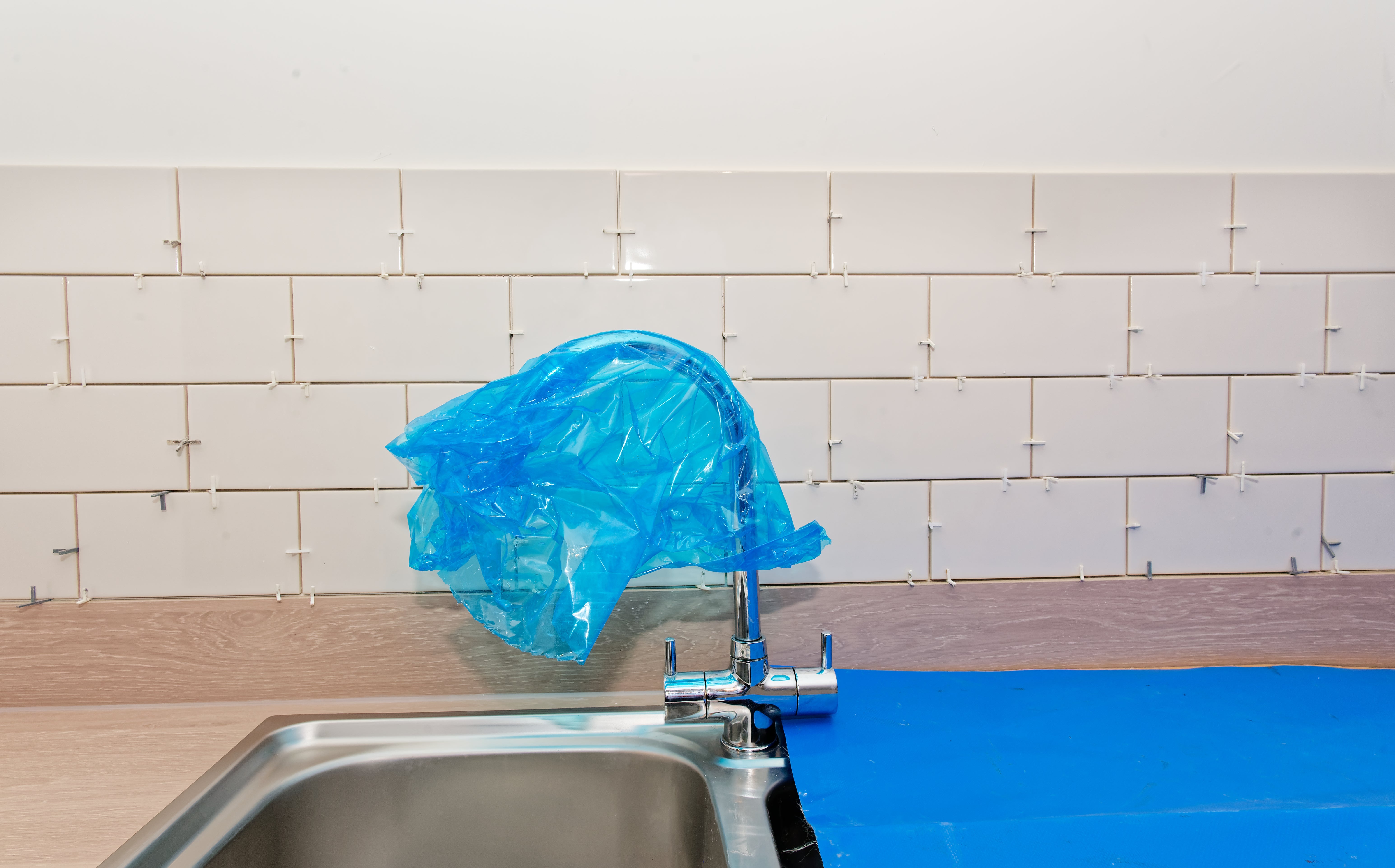 Plastic wrapper  covers a room  faucet, protecting it during renovation work. Tiles down  are partially installed