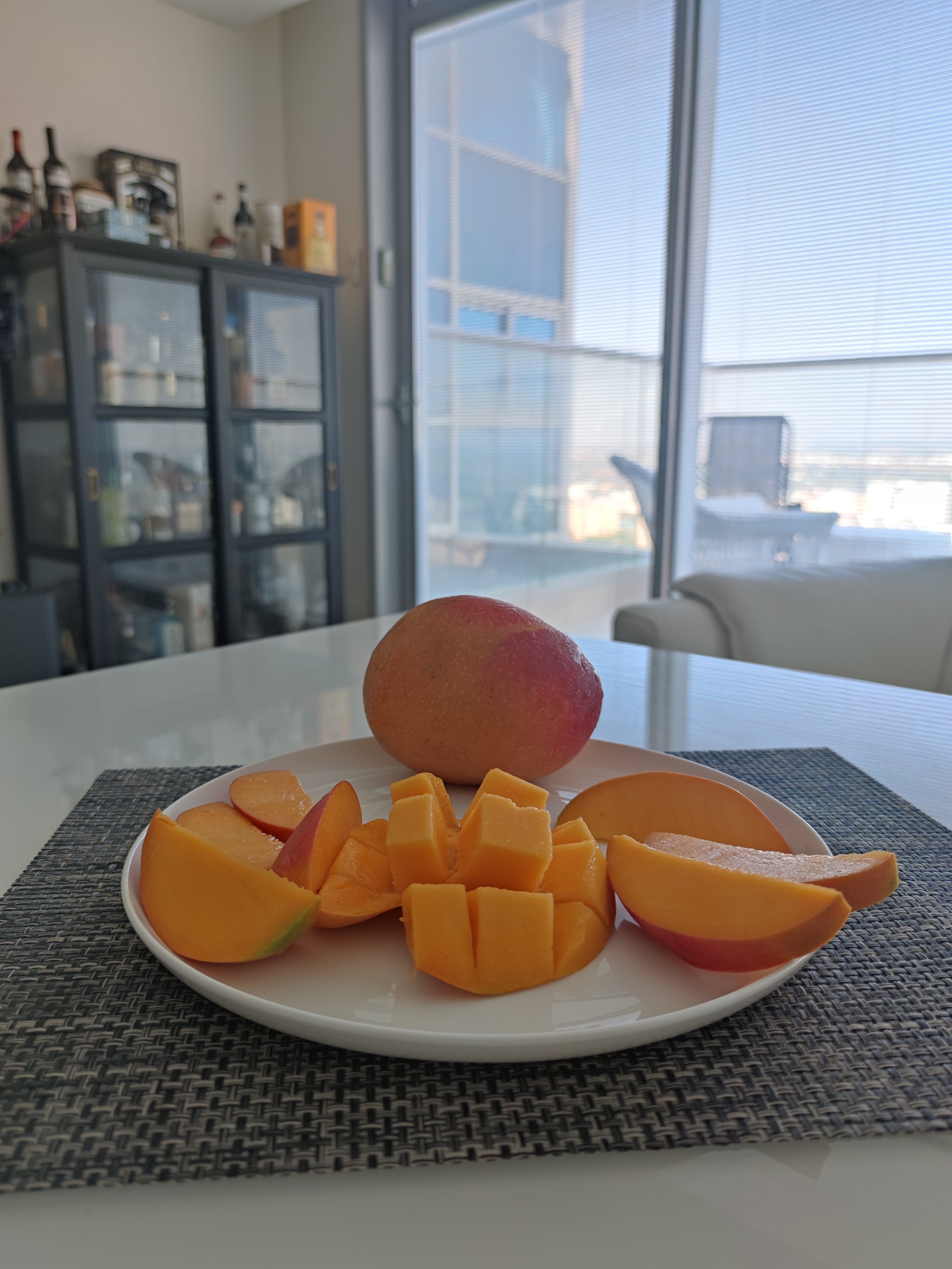 A sheet  with sliced and cubed mango sits connected  a placemat successful  a modern   room  with a solid  furniture  and ample  windows successful  the background