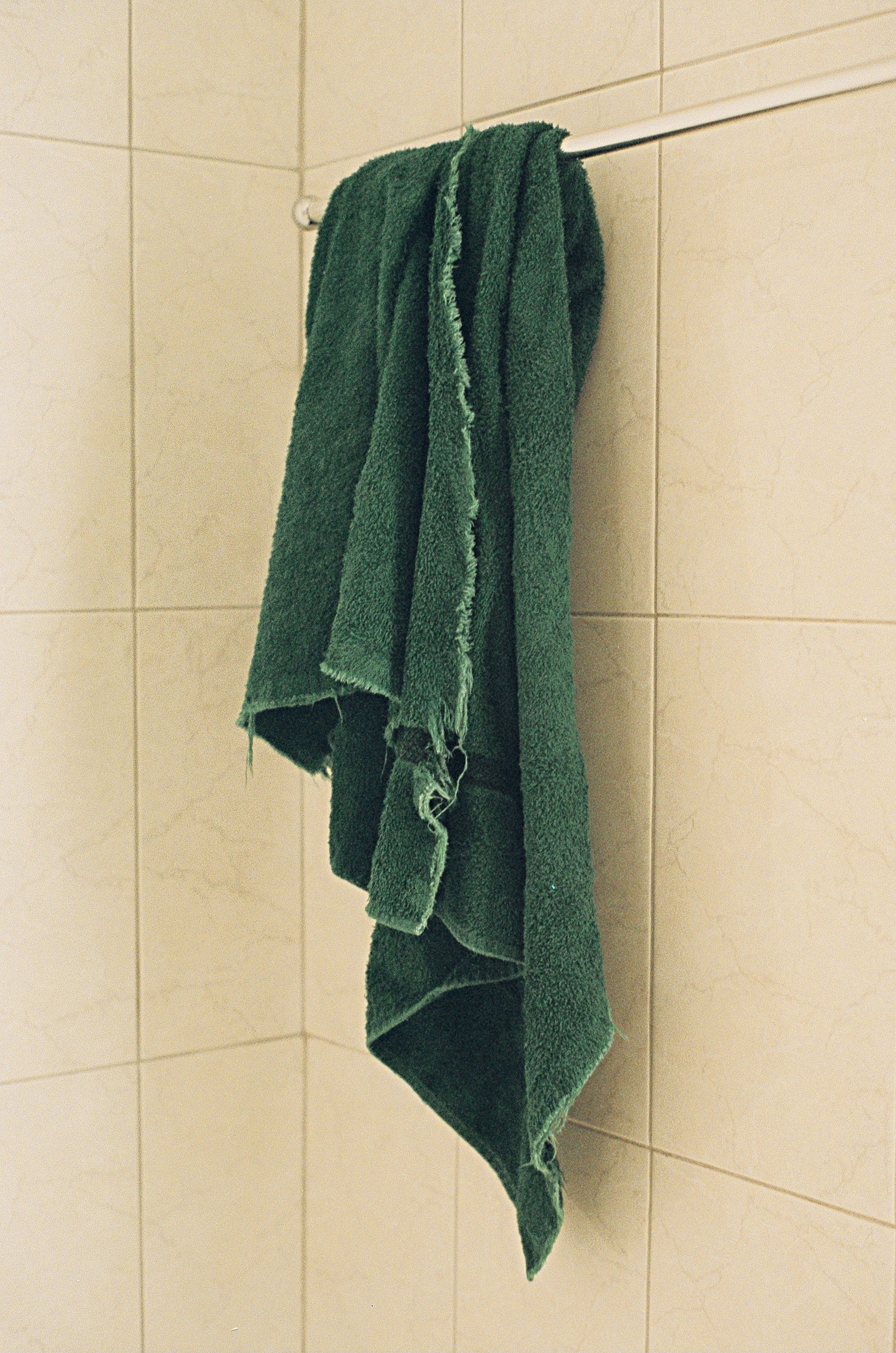 A greenish  towel hangs connected  a metallic  barroom  against a tiled wall