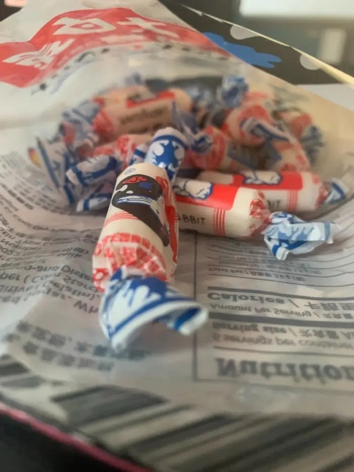Open container  of wrapped candies scattered connected  newspaper, displaying vintage-style packaging