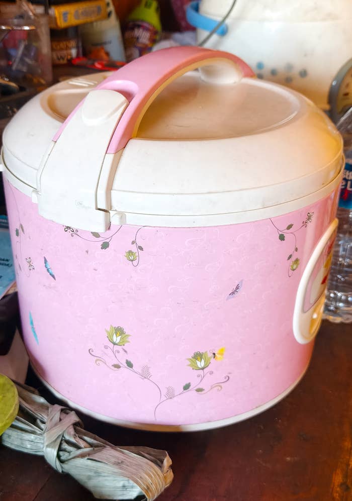 A pinkish  atom   cooker with floral plan  connected  a cluttered room  counter