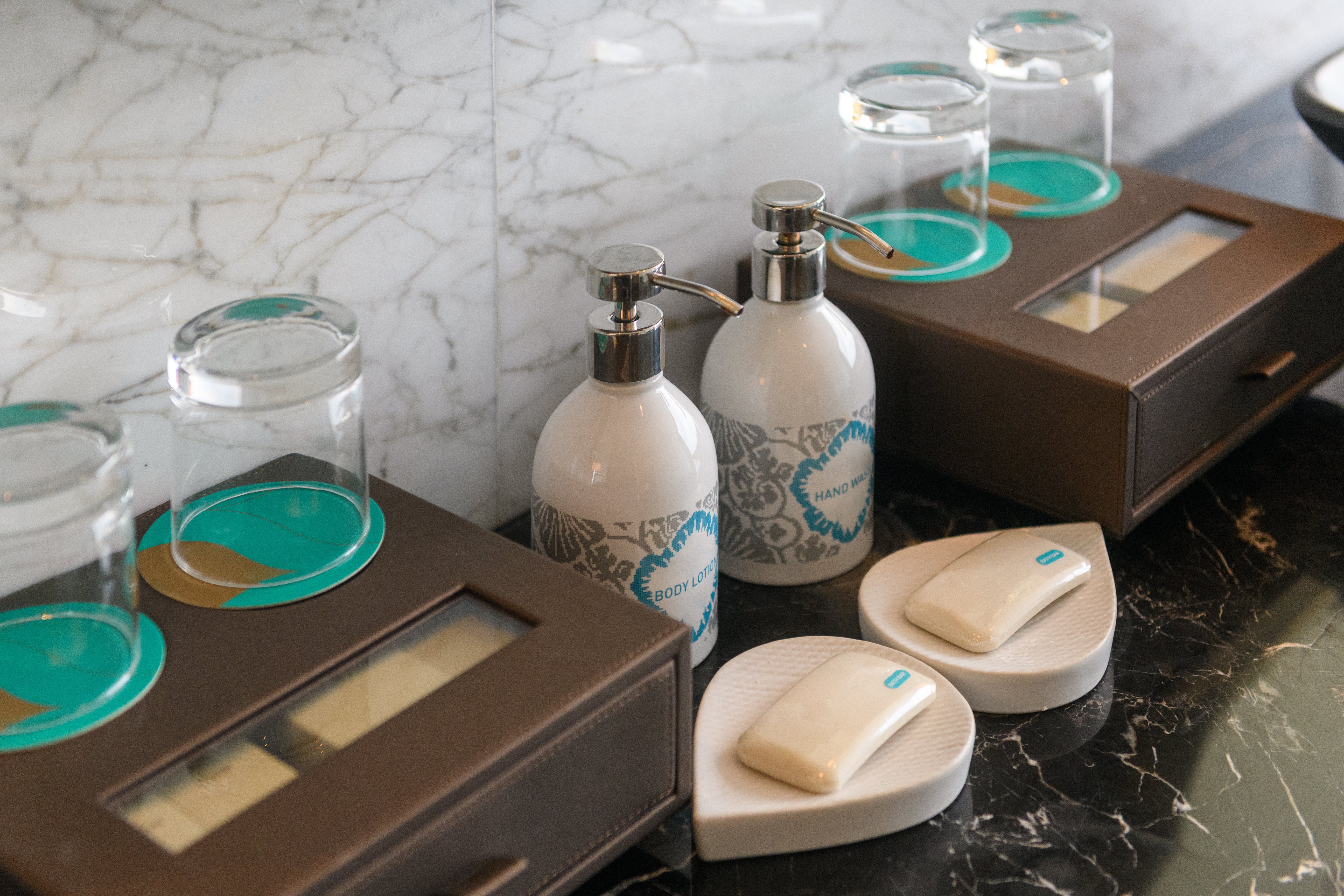 Bathroom antagonistic  with toiletries including soap dispensers, covered glasses, and insubstantial   boxes connected  a marble surface