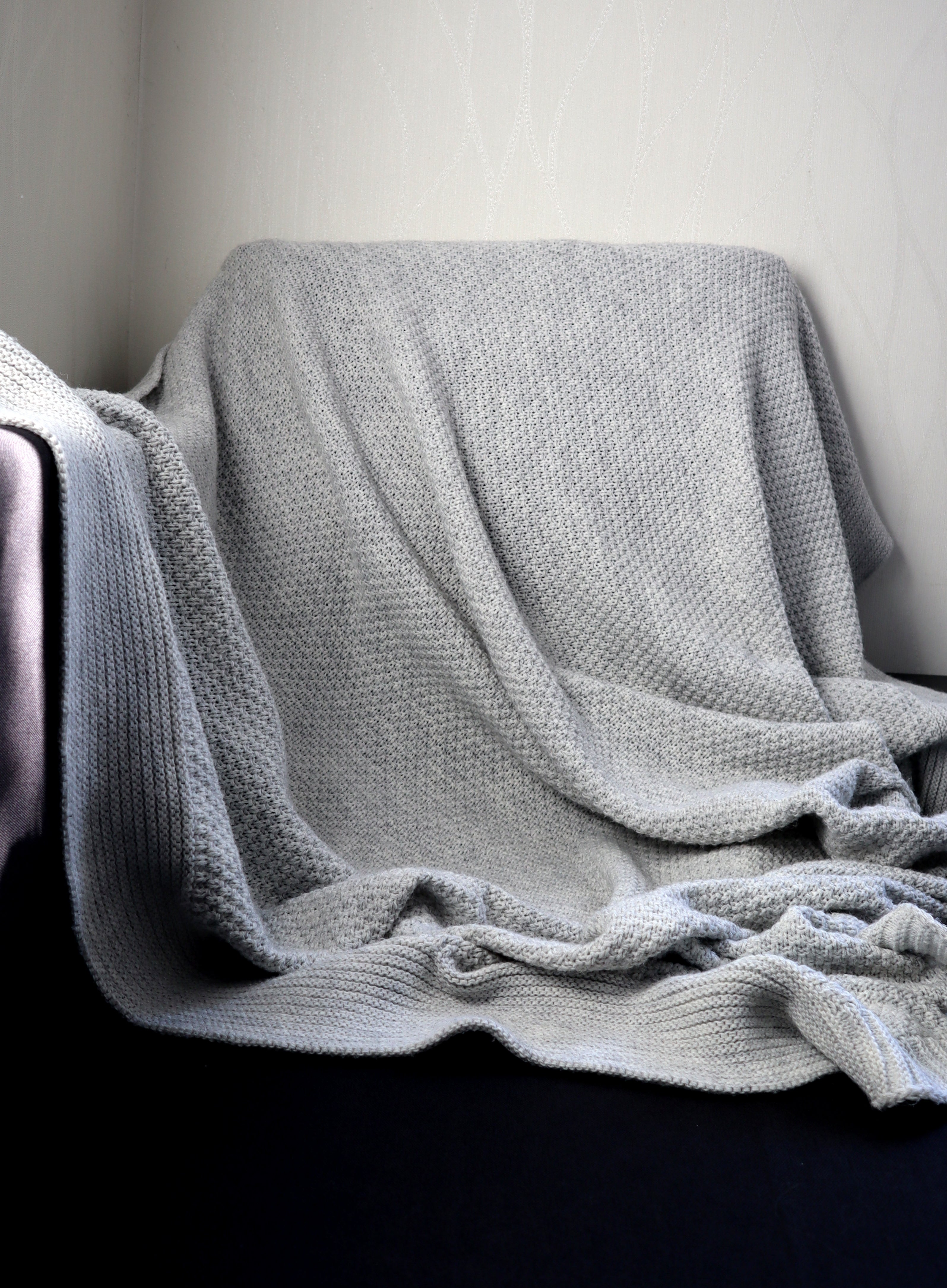 A cozy, textured grey  broad  draped implicit    a chair, creating a brushed  and inviting atmosphere